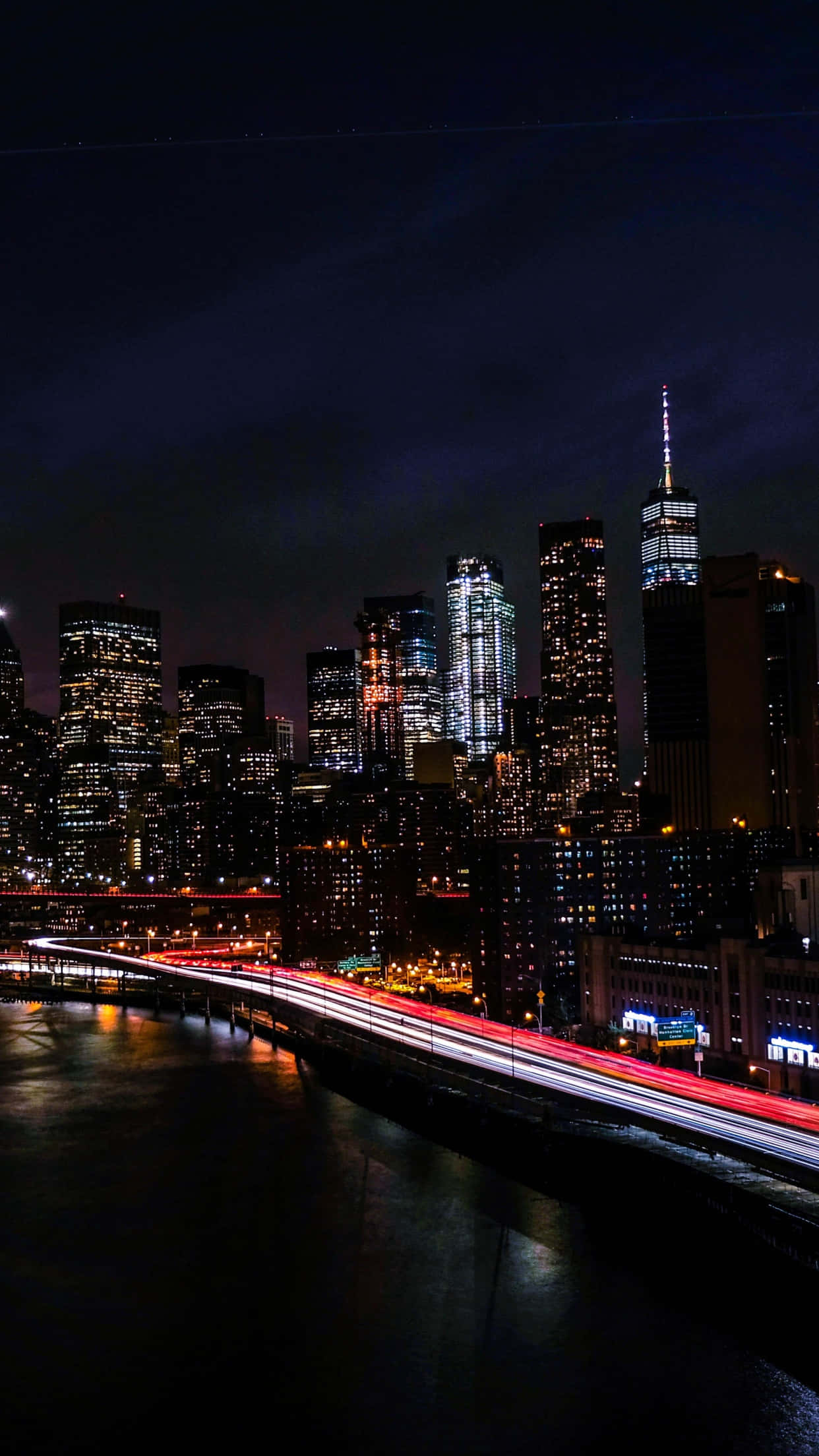 New York City Night iPhone 桌布 壁紙 — 紐約充滿活力的夜景，閃爍的摩天大樓和水面上劃過的紅色交通燈光。