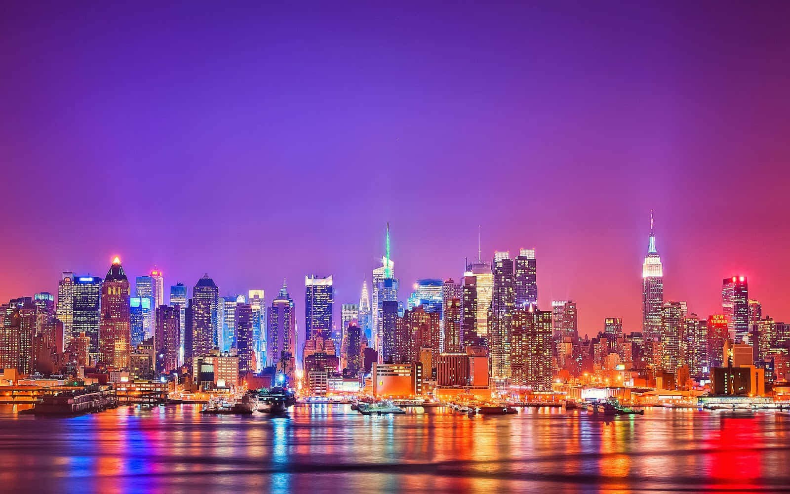 New York 桌布 壁紙 — 紐約充滿活力的夜景，閃爍的摩天大樓在紫色和粉紅色的天空下倒映在水中。