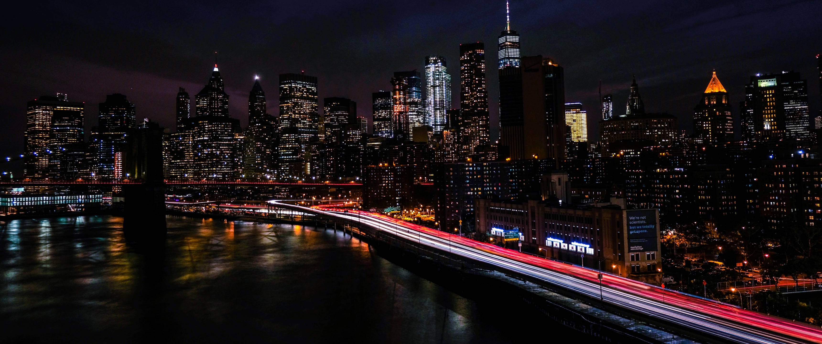 New York 桌布 壁紙 — 紐約充滿活力的夜景，閃爍的摩天大樓和水上橋樑上劃過的紅色交通燈光。