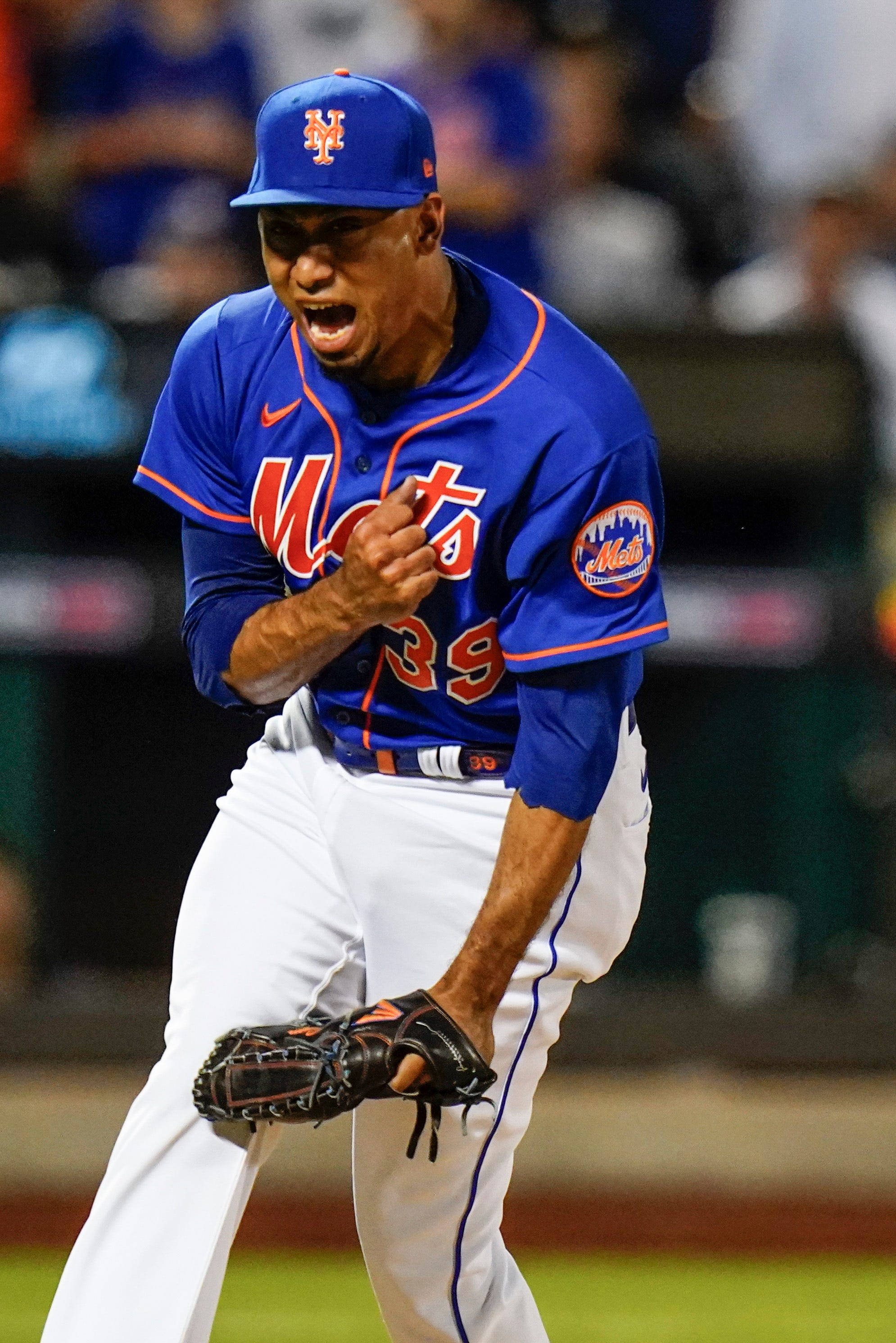 MLB Players 桌布 壁紙 — 紐約大都會棒球投手身穿藍色和橙色球衣，在夜間比賽的球場燈光下激烈咆哮。