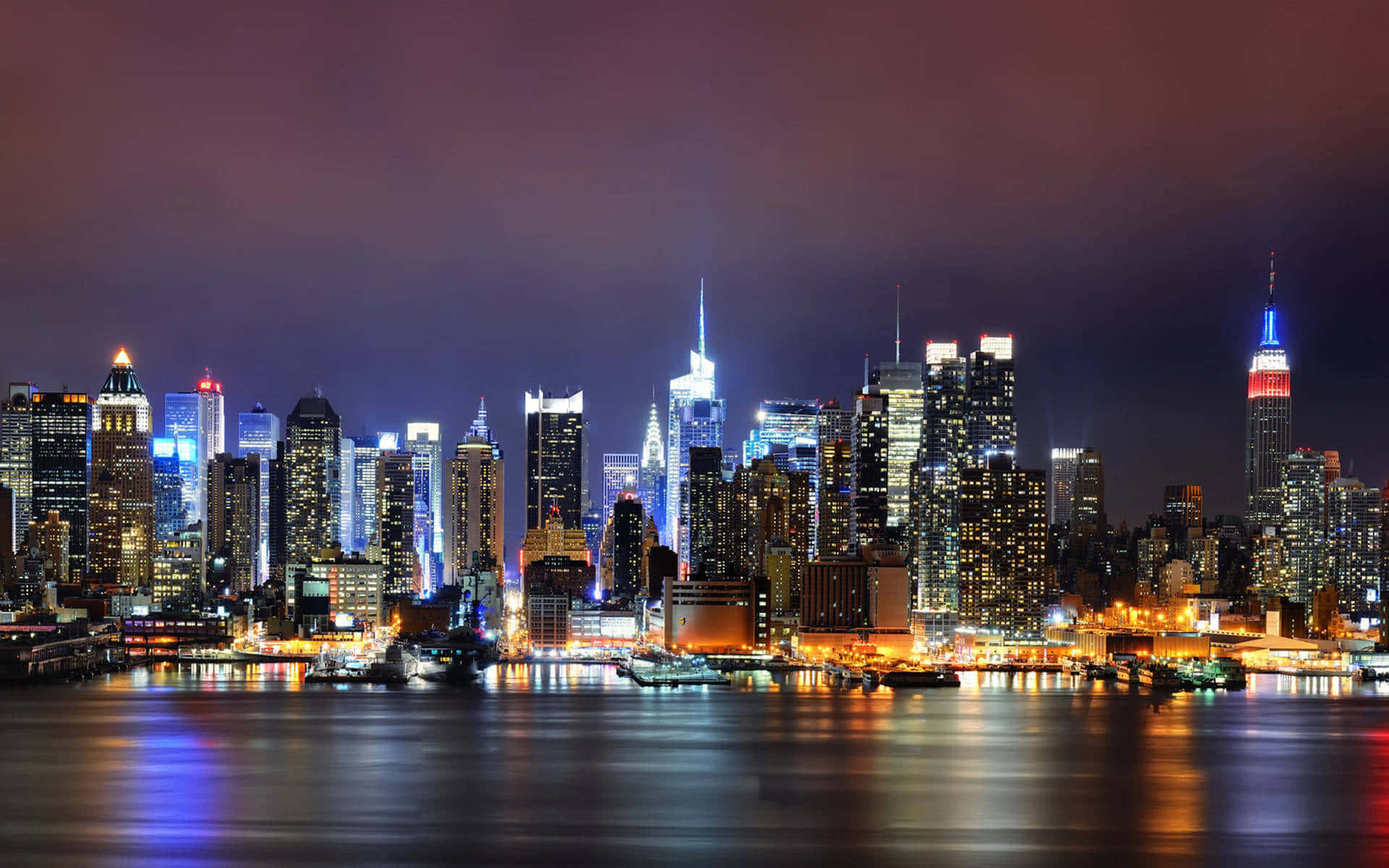 Buildings 桌布 壁紙 — 紐約天際線的璀璨夜景，發光的摩天大樓倒映在平靜的水面上。