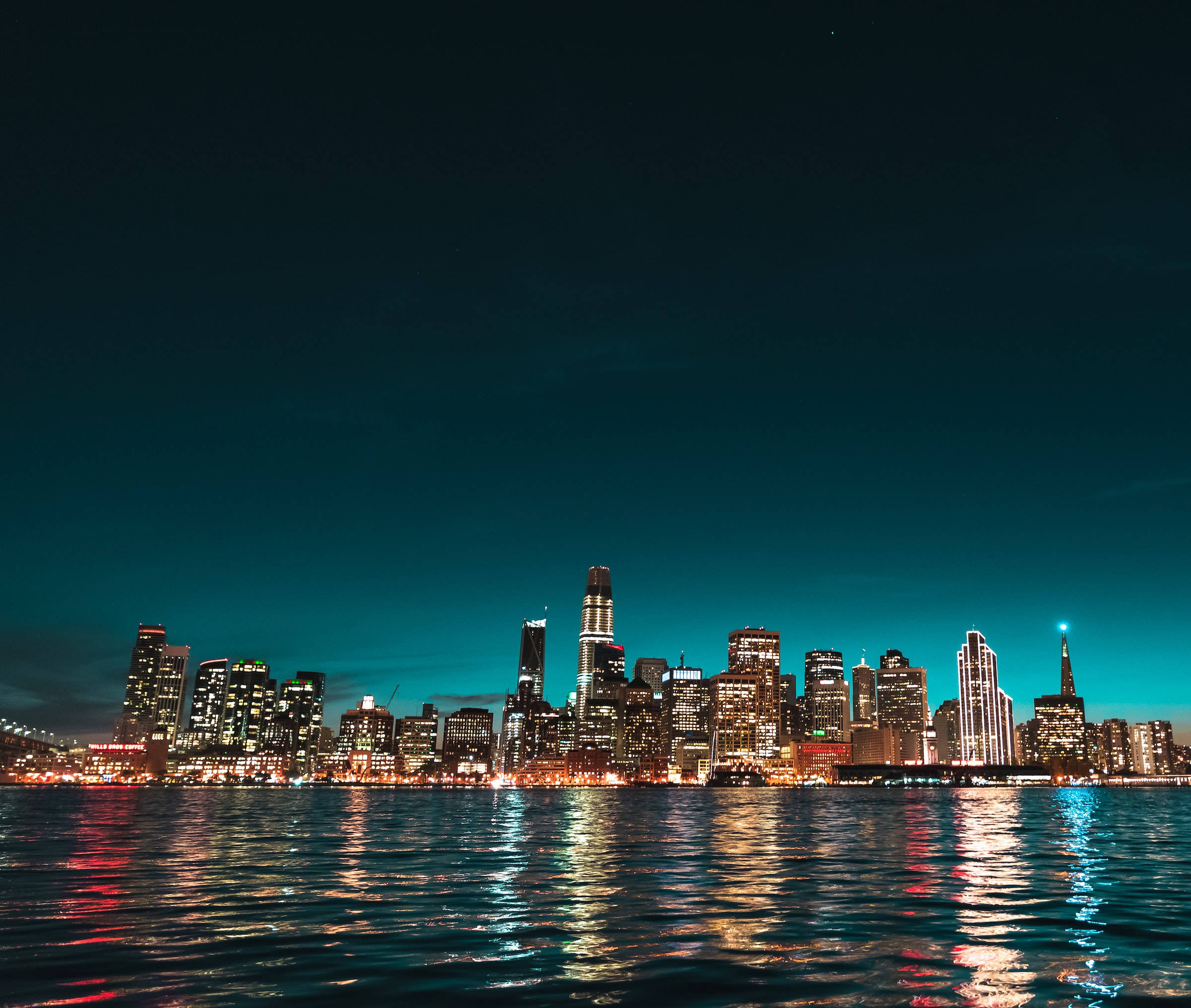 Night Aesthetic 桌布 壁紙 — 紐約天際線的絕美夜景，閃爍的摩天大樓倒映在深色水面上，天空呈現深藍綠色。