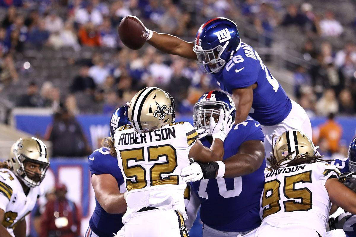 Saquon Barkley 桌布 壁紙 — 紐約巨人隊球員跳起接住美式足球，同時紐奧良聖徒隊防守球員在夜間比賽中對他進行擒抱。