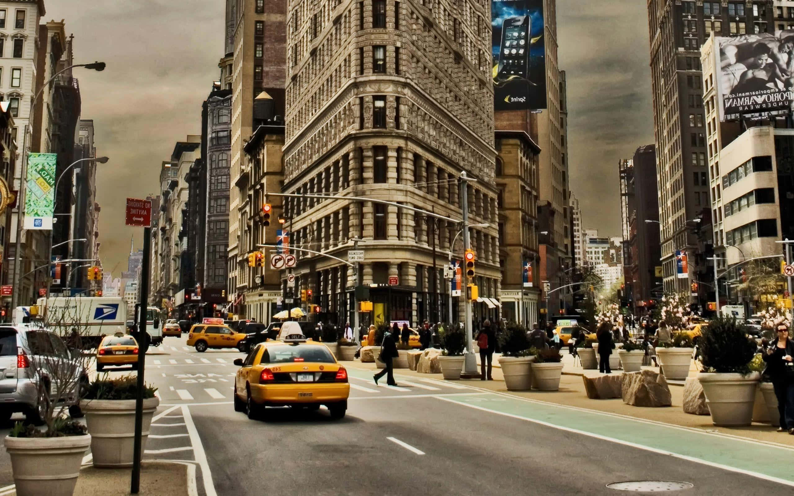New York 桌布 壁紙 — 紐約市一個繁忙的街角，有黃色計程車、行人和歷史建築，天空多雲。