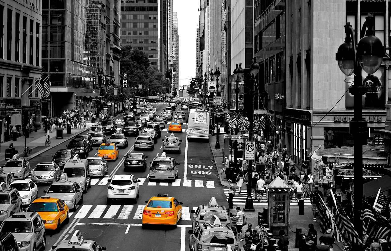 New York 桌布 壁紙 — 紐約市一條繁忙的街道，充滿活力的黃色計程車和行人在高聳的建築物和美國國旗之間穿梭。