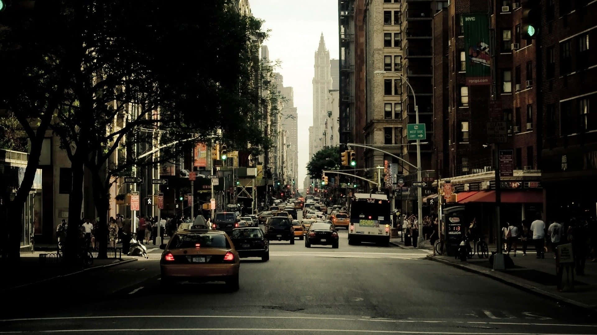 City Street 桌布 壁紙 — 紐約市一條繁忙的街道，兩旁高樓大廈和樹木林立，汽車和行人絡繹不絕，天空朦朧。