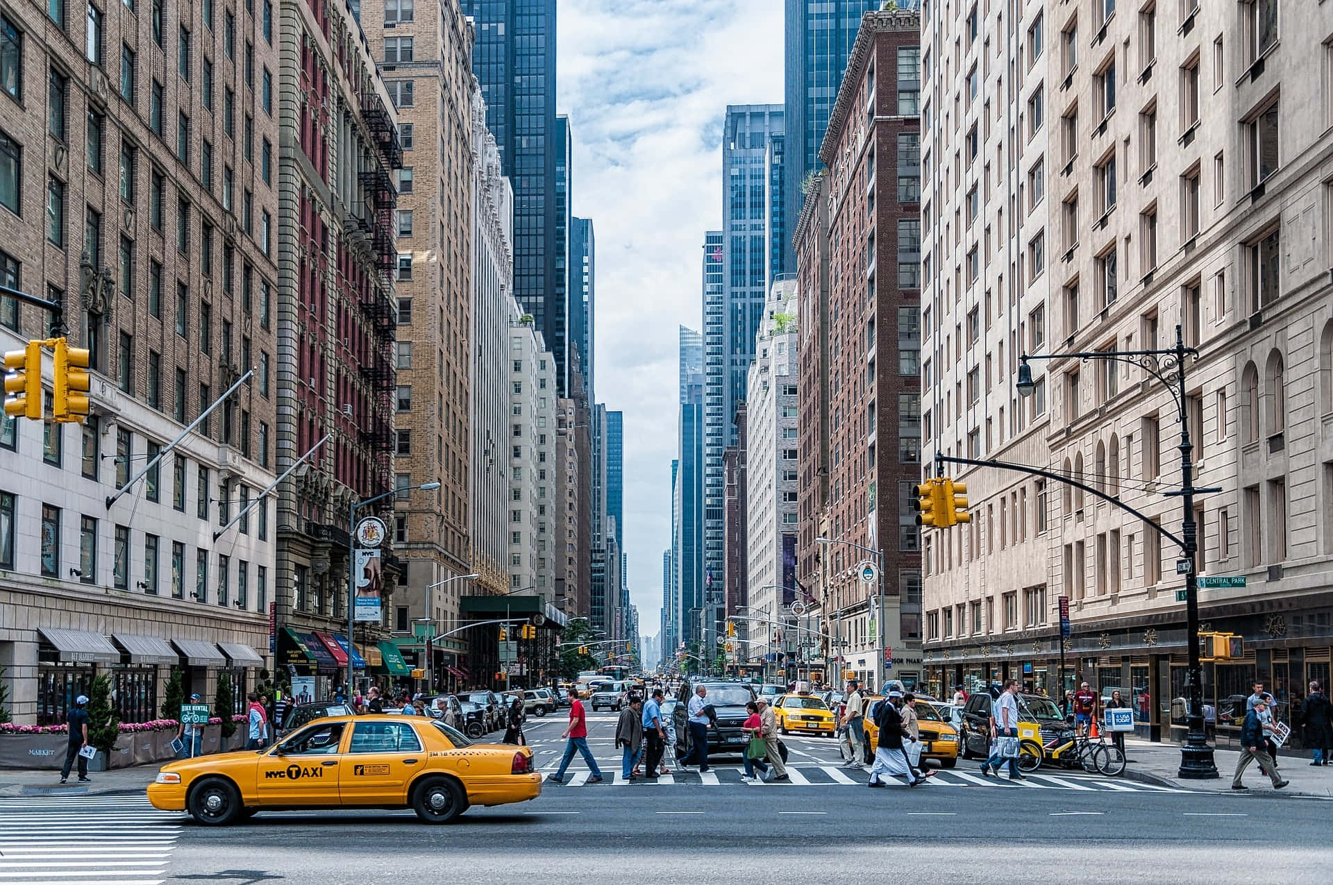 Nyc 桌布 壁紙 — 紐約市一條繁忙的街道，黃色計程車和行人在高聳的歷史與現代建築之間穿行，天空部分多雲。