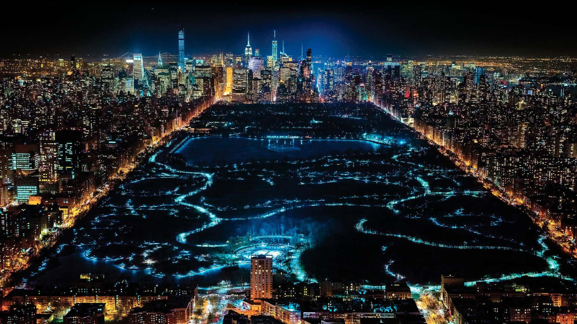 紐約市 桌布 壁紙 — 紐約市中央公園的夜間鳥瞰圖，藍色燈光蜿蜒穿過小徑和湖泊，周圍環繞著高聳的摩天大樓。