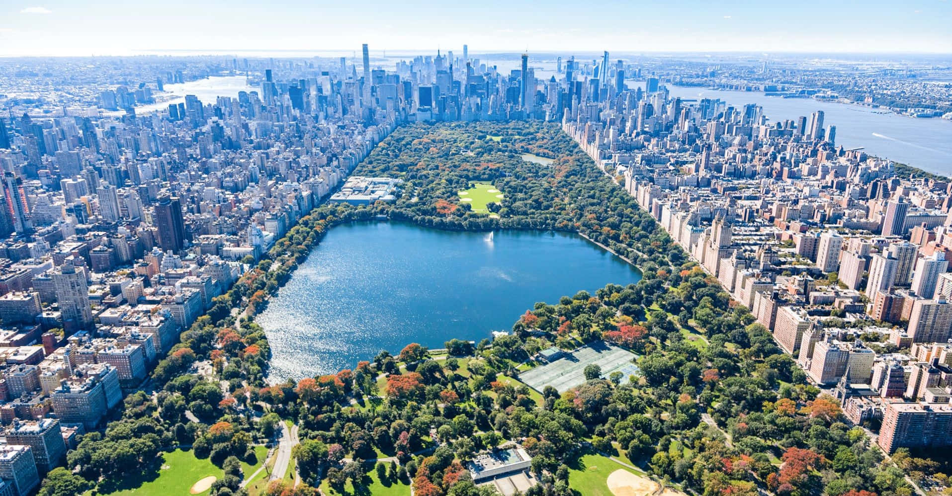 New York 桌布 壁紙 — 紐約市中央公園的鳥瞰圖，周圍環繞著摩天大樓和秋樹，天空清澈湛藍。