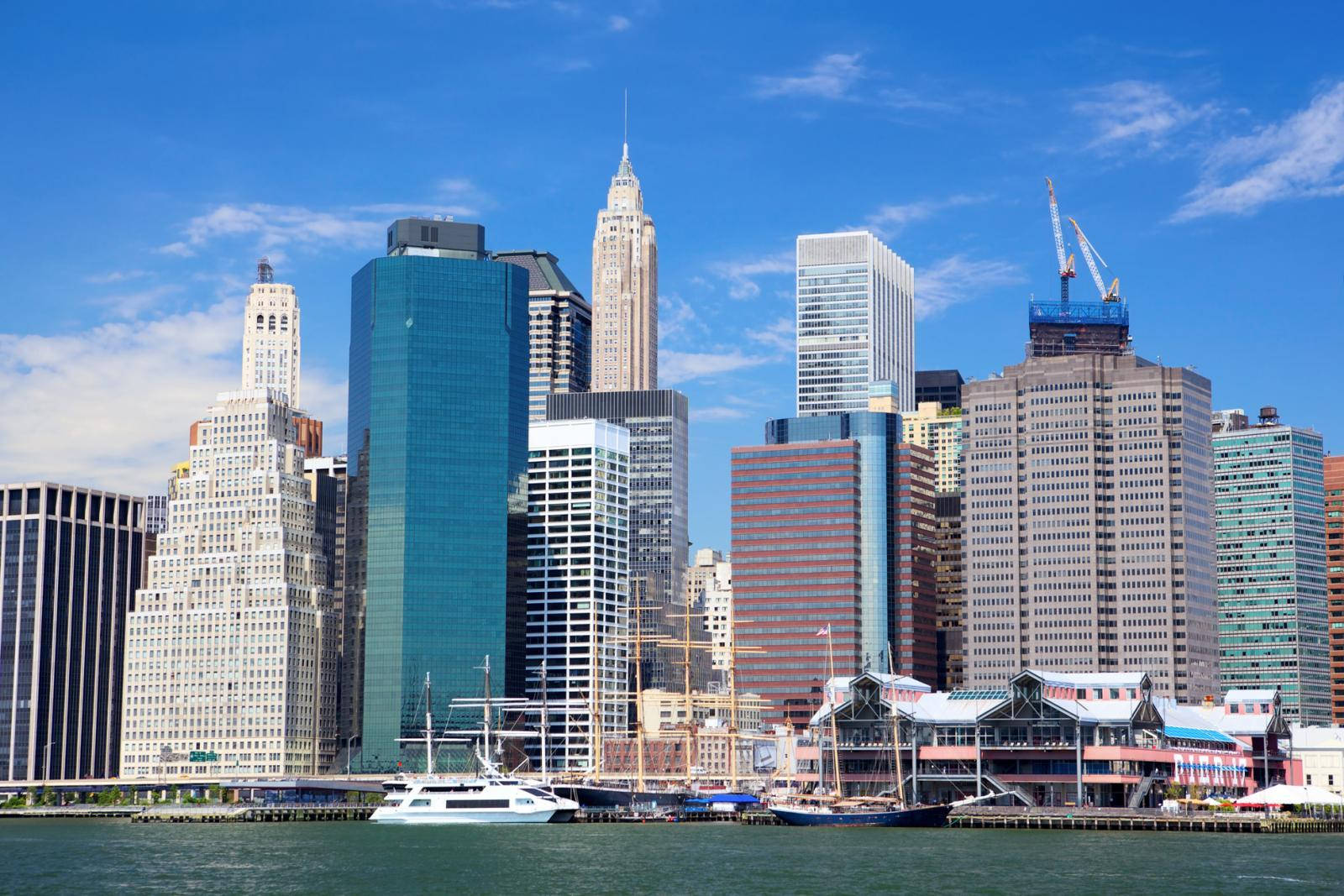 New York 桌布 壁紙 — 紐約市充滿活力的日間天際線，高聳的摩天大樓映照著藍天，船隻停泊在海濱。