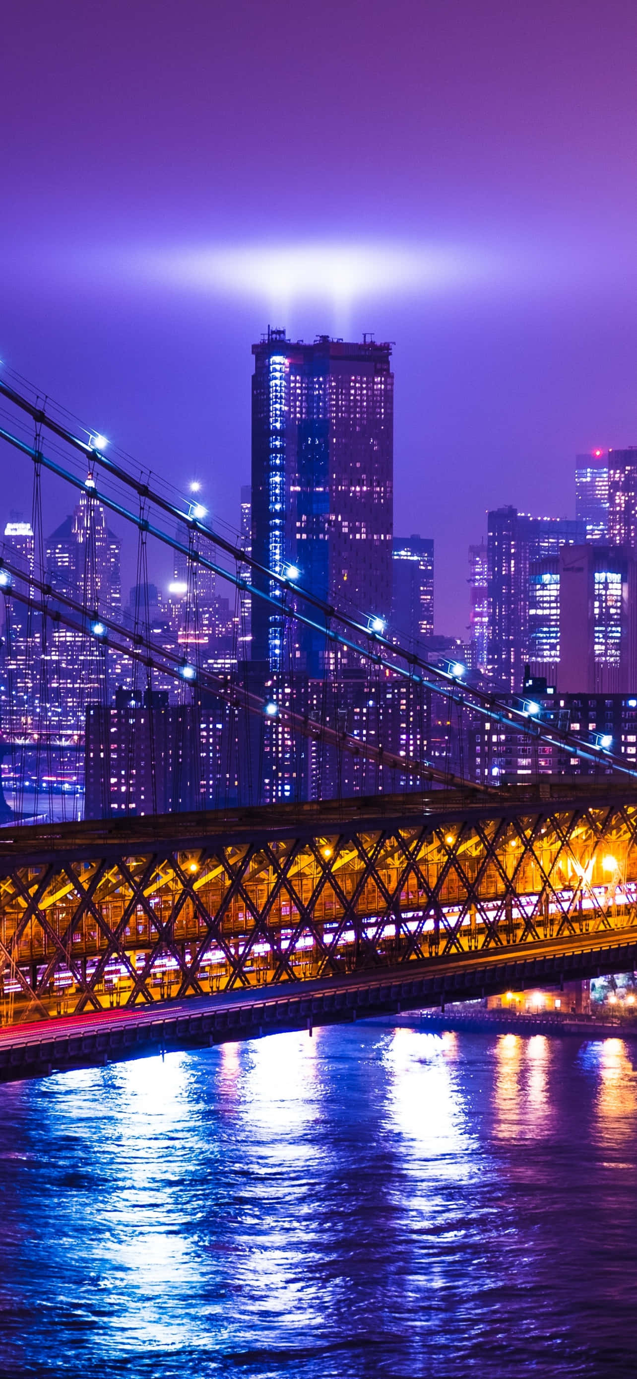 New York City Night iPhone 桌布 壁紙 — 紐約市充滿活力的紫色暮色天際線，布魯克林大橋在發光的水面上照亮。