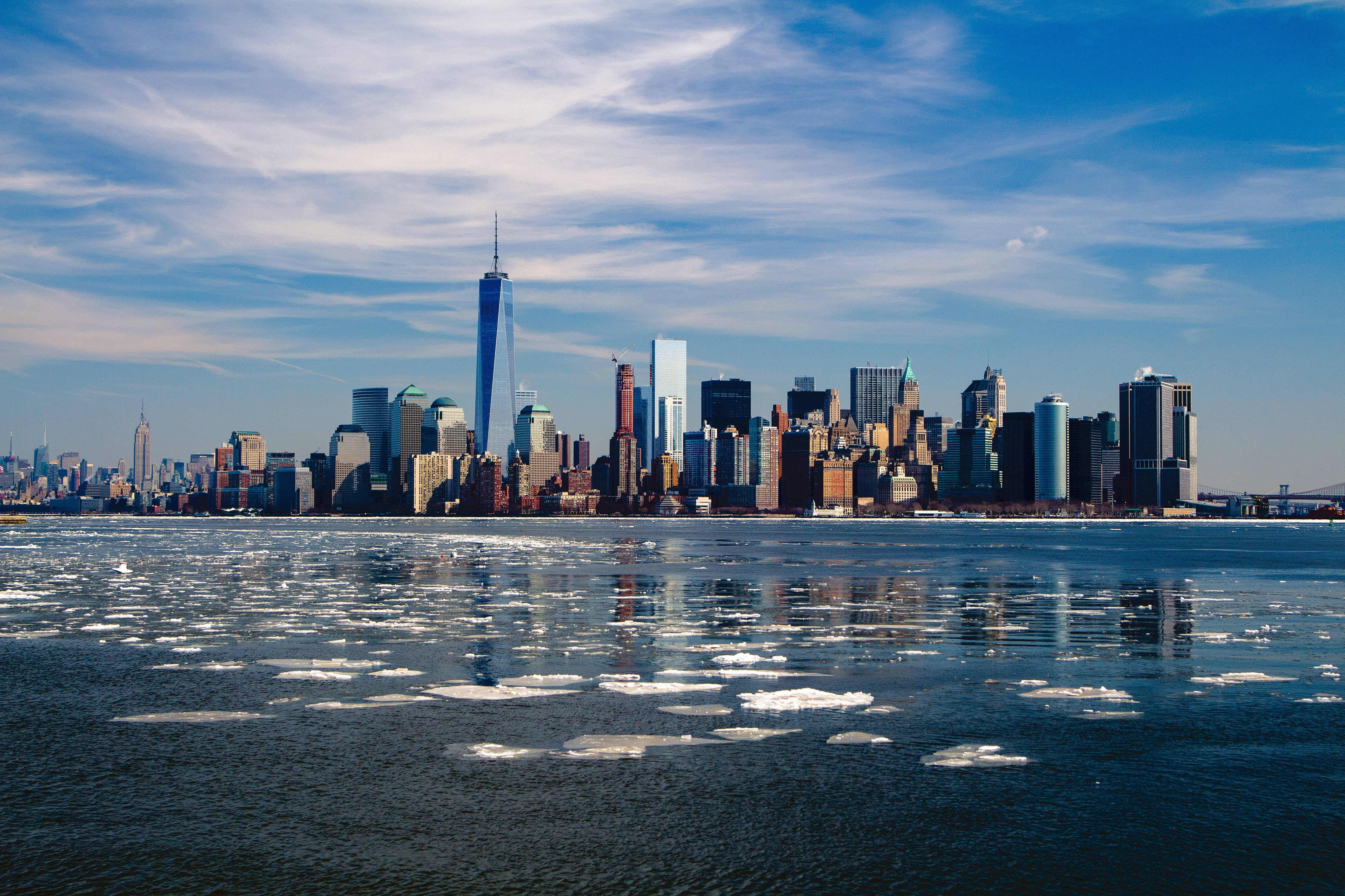 Nyc Aesthetic 桌布 壁紙 — 紐約市天際線，One World Trade Center 塔樓倒映在冰冷的水中，天空湛藍，白雲輕柔。