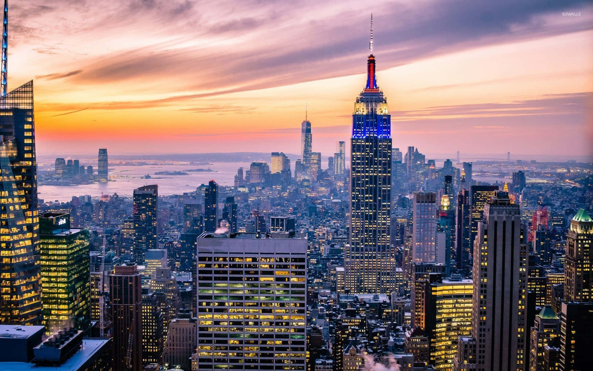Nyc 桌布 壁紙 — 紐約市天際線上的壯麗日落，帝國大廈閃爍著藍光，上方有橙色雲彩。