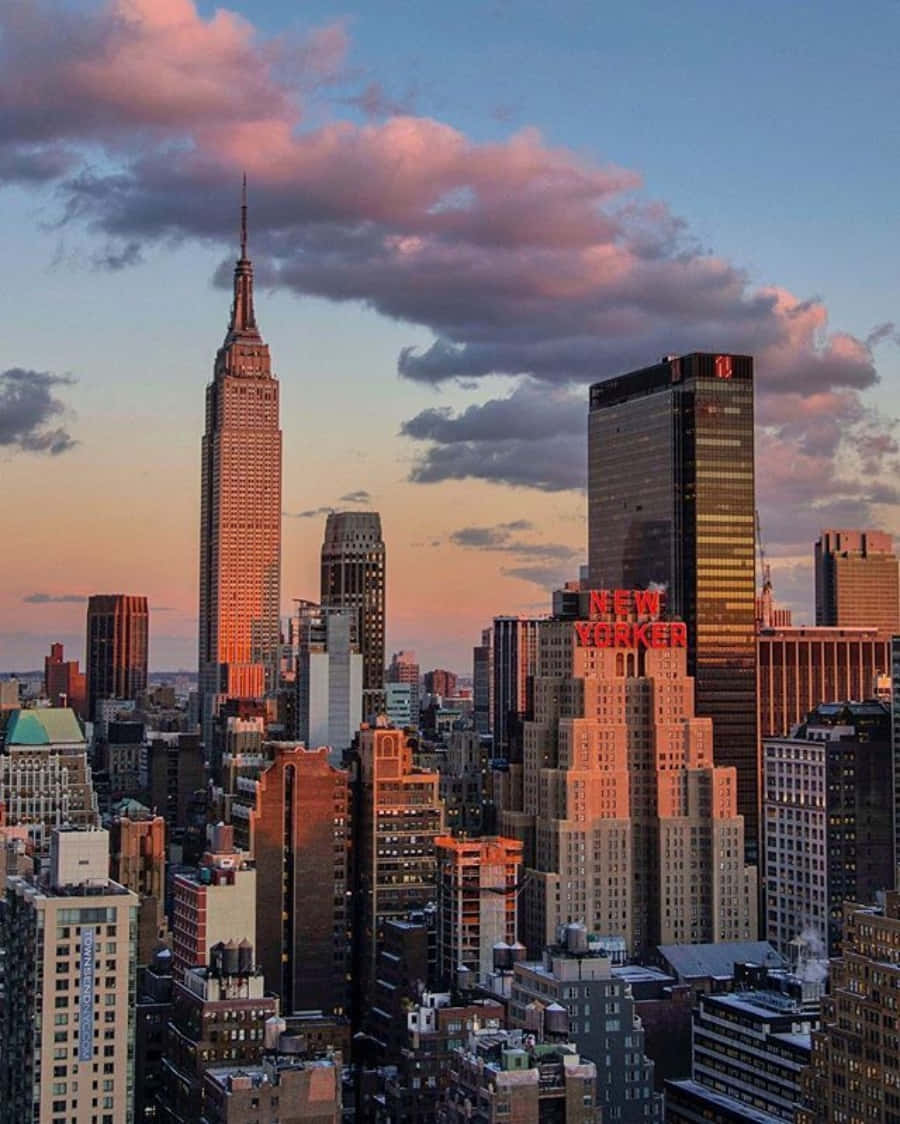 Nyc Aesthetic 桌布 壁紙 — 紐約市天際線在日落時分，帝國大廈在粉紅雲朵下閃耀琥珀色光芒。