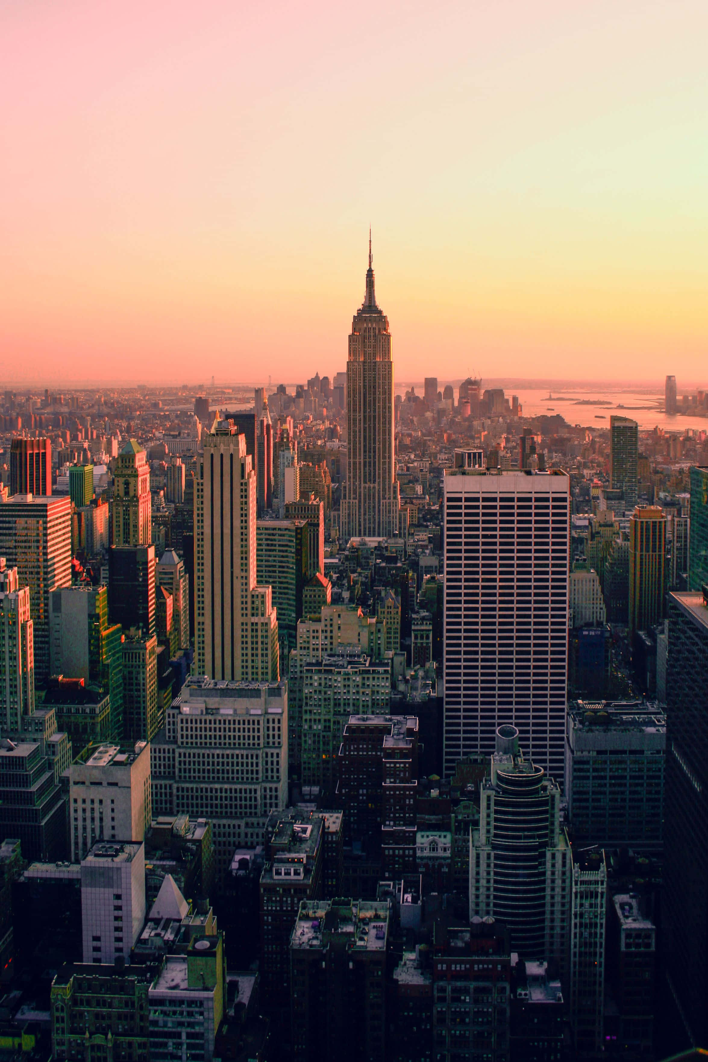 Nyc Aesthetic 桌布 壁紙 — 紐約市天際線在日落時的鳥瞰圖，帝國大廈在粉紅色和橙色的天空中閃耀。