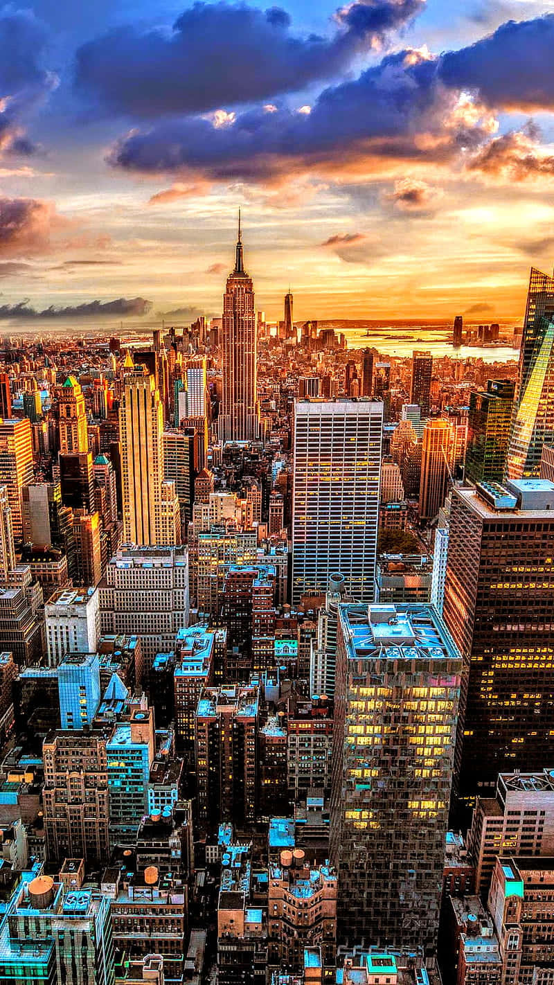 New York City 4K Ultra HD 桌布 壁紙 — 紐約市天際線在日落時的鳥瞰圖，帝國大廈聳立在發光的摩天大樓和戲劇性的橙紫色雲層之上。