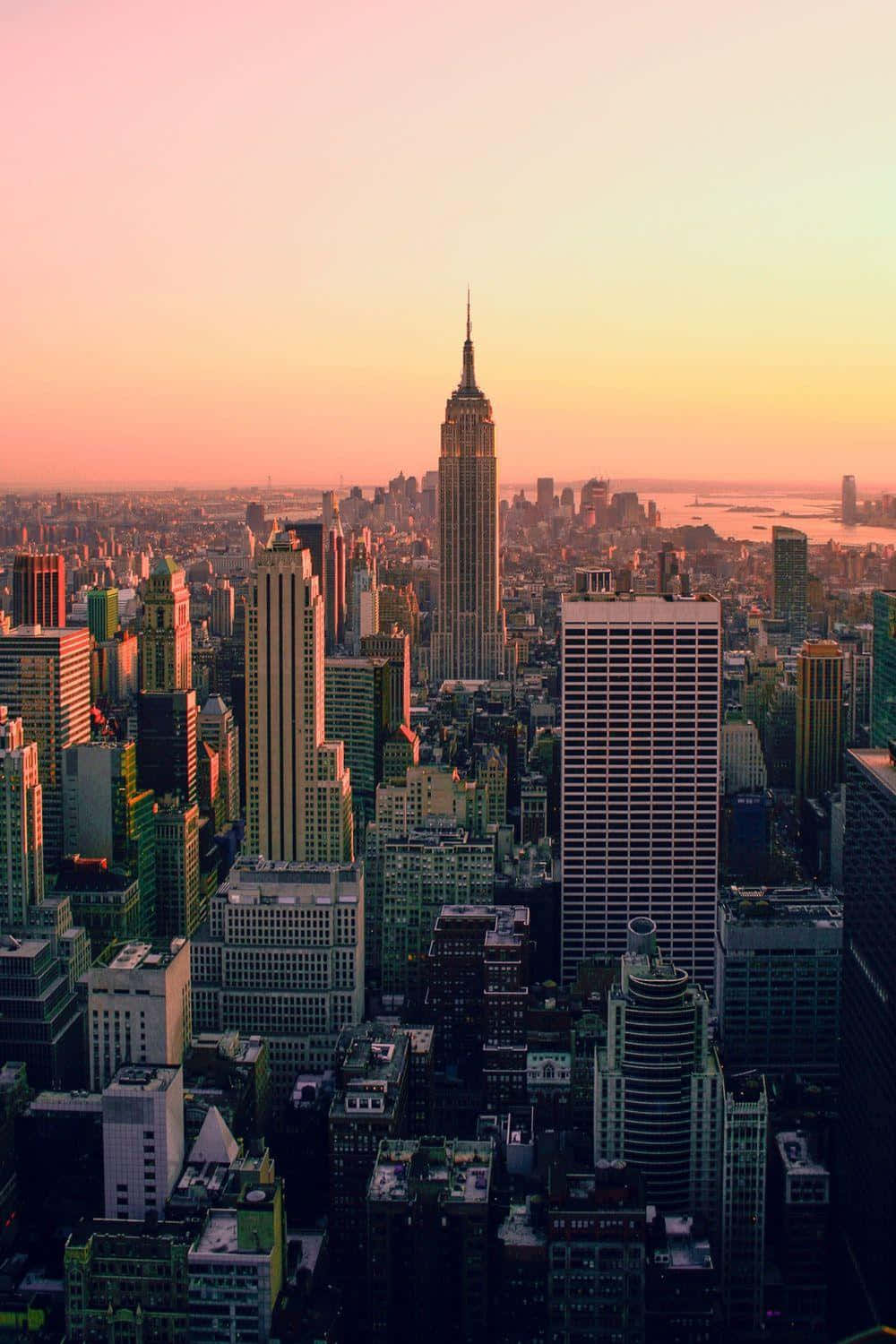 New York 桌布 壁紙 — 紐約市天際線在日落時的鳥瞰圖，帝國大廈在粉紅色和橙色的天空中閃耀。