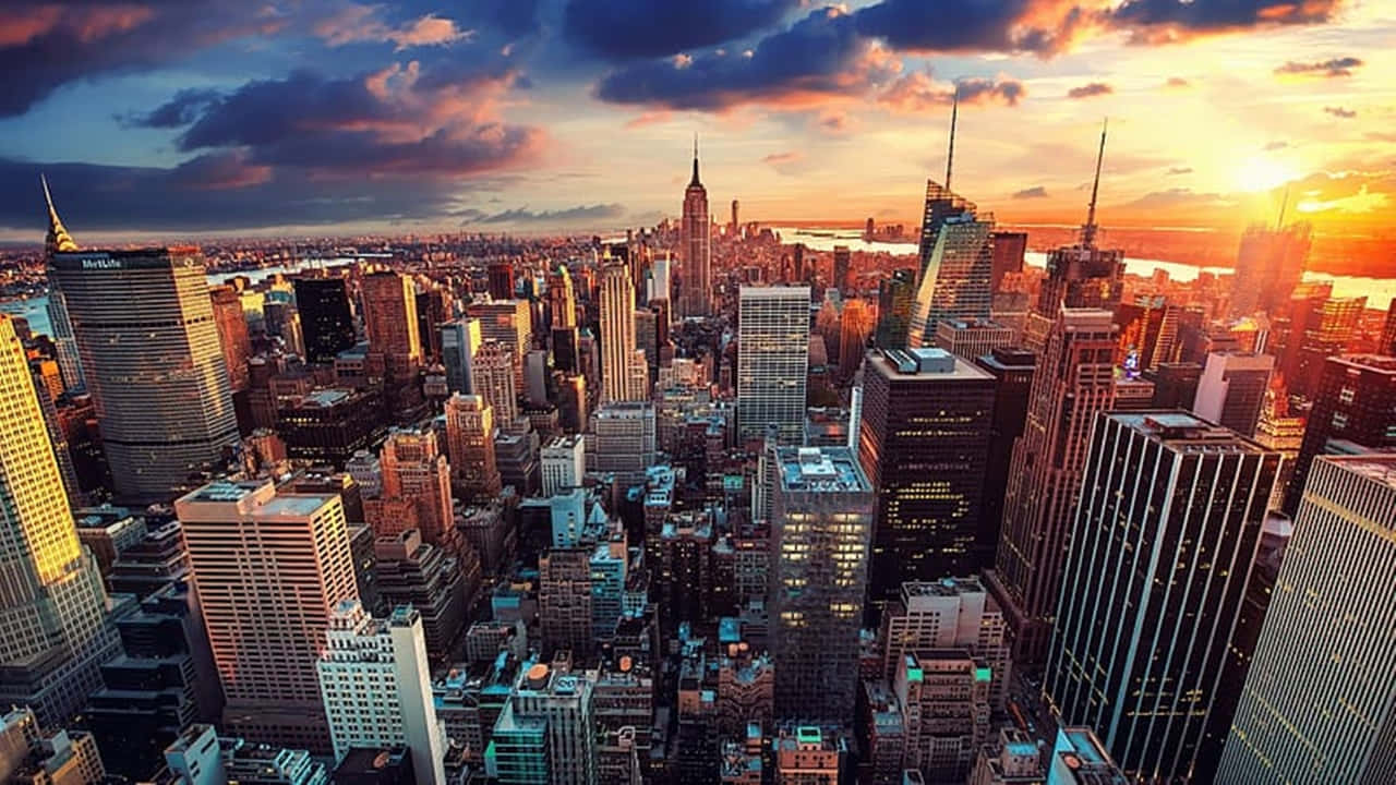 720p Ny City 桌布 壁紙 — 紐約市天際線在日落時的鳥瞰圖，金色光線照亮摩天大樓和戲劇性的雲層。