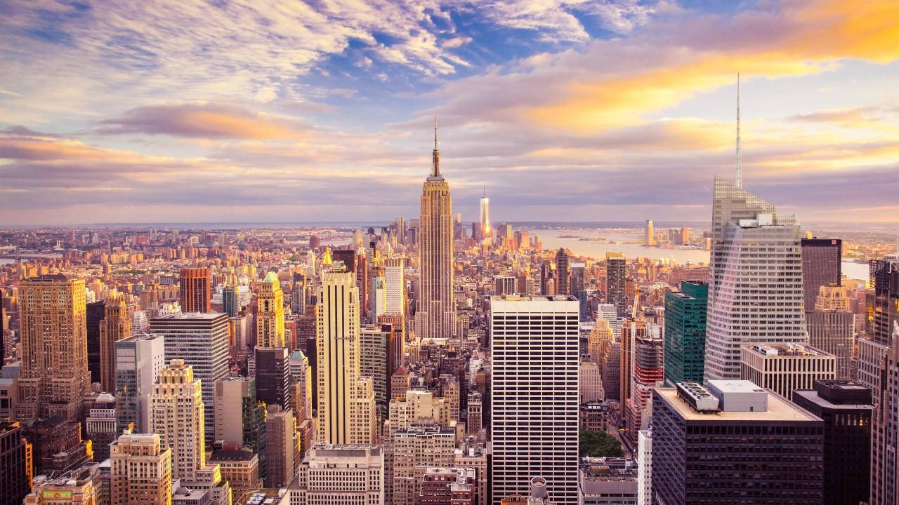 New York 桌布 壁紙 — 紐約市天際線在日落時的鳥瞰圖，金色光芒照亮摩天大樓和雲層。