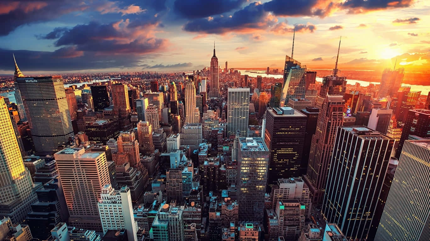 1366x768 Empire State Building 桌布 壁紙 — 紐約市天際線在日落時的鳥瞰圖，金色光線照亮摩天大樓和戲劇性的雲層。