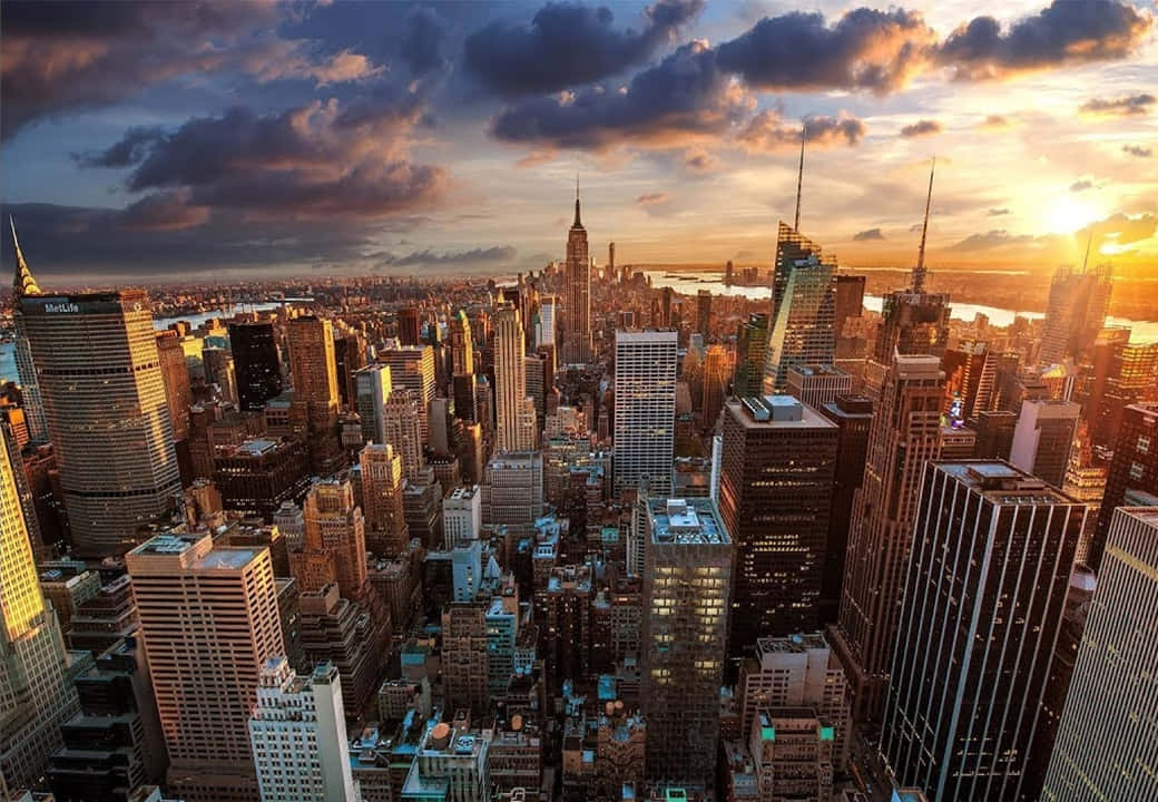 720p Ny City 桌布 壁紙 — 紐約市天際線在日落時的鳥瞰圖，金色光線照亮摩天大樓和戲劇性的雲層。