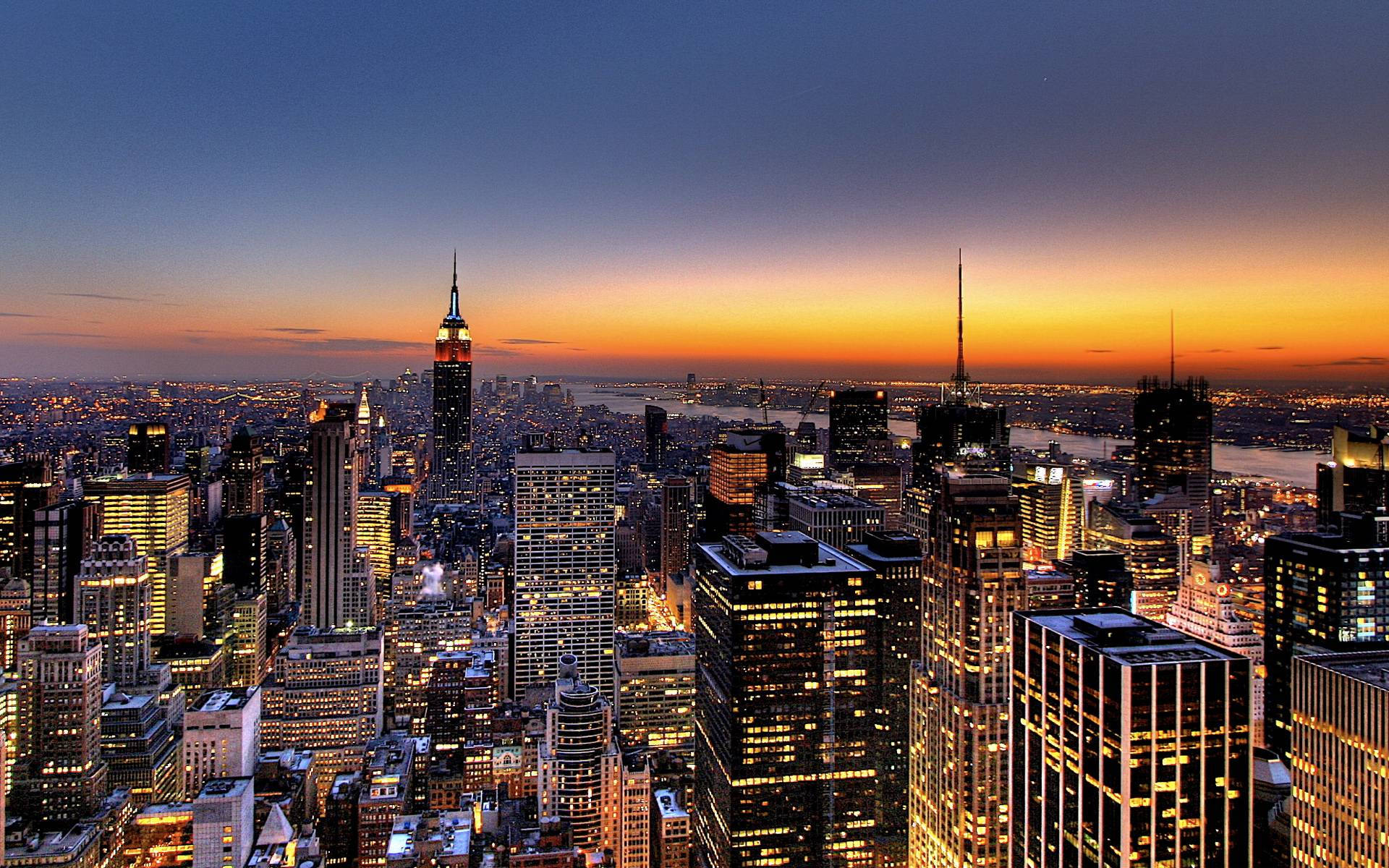 Skyscraper 桌布 壁紙 — 紐約市天際線在暮色中的壯麗景色，摩天大樓在橙藍漸變的天空下閃閃發光。