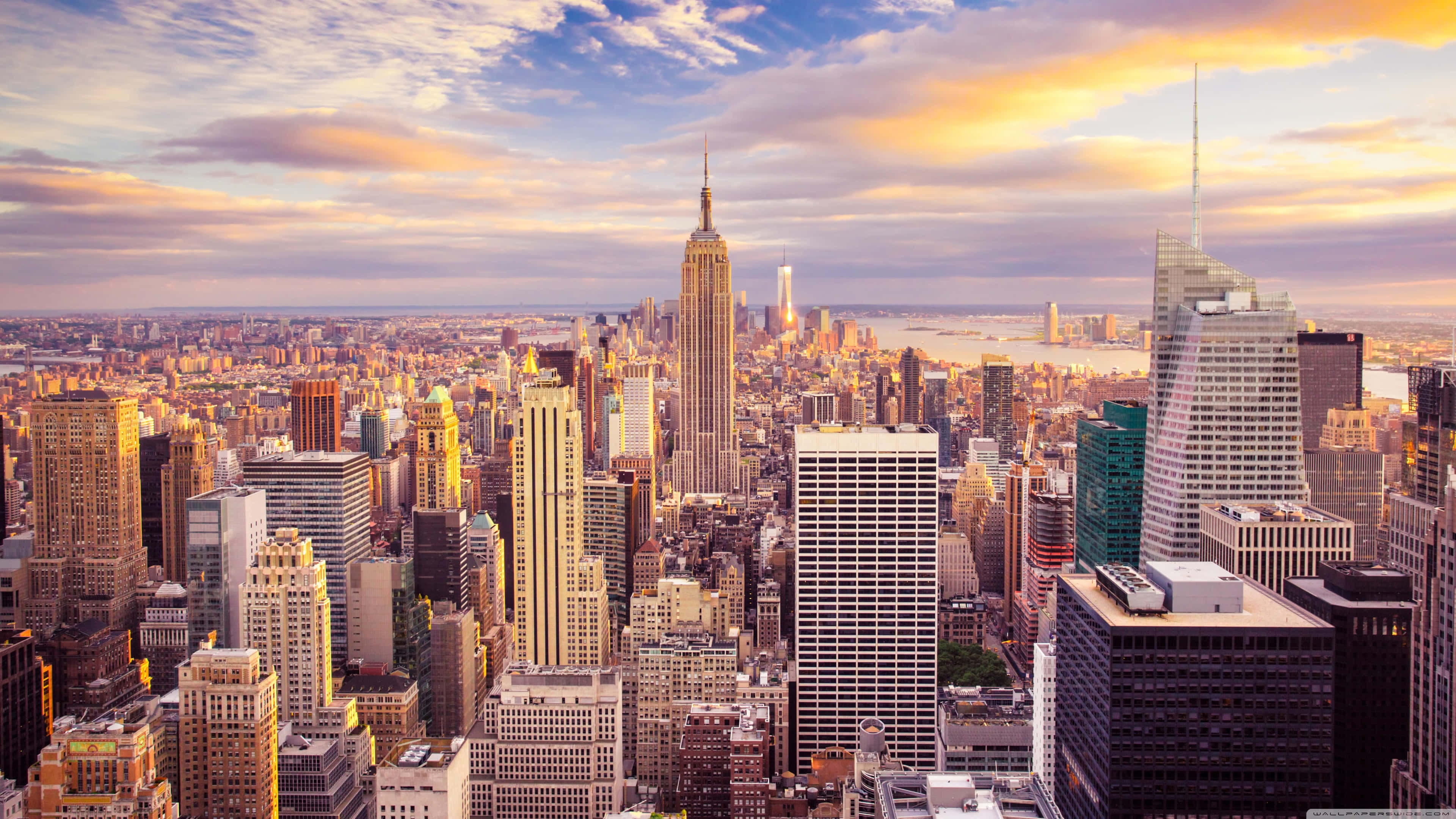 New York City 4K Ultra HD 桌布 壁紙 — 紐約市天際線在金色日落下的壯麗鳥瞰圖，帝國大廈聳立在密集的摩天大樓和朦朧雲霧之上。