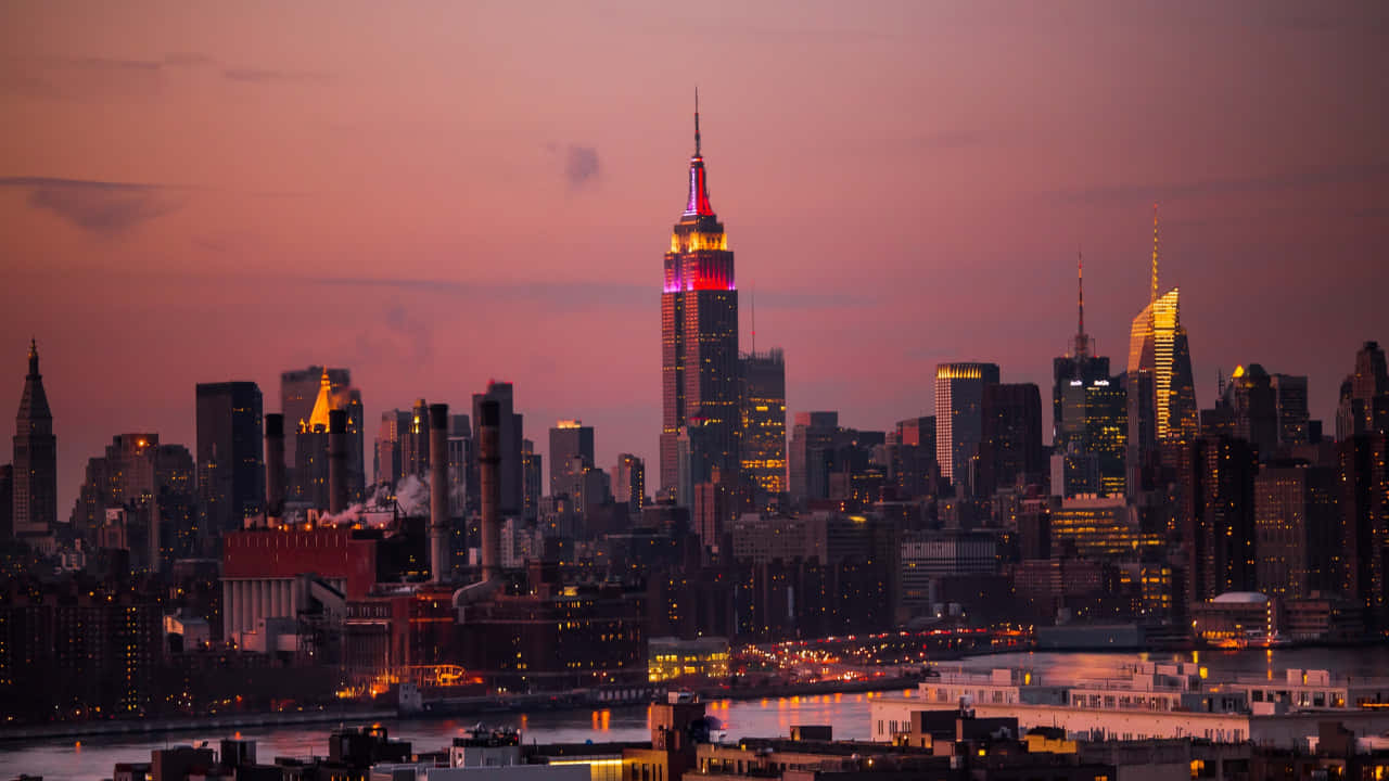 720p Empire State Building 桌布 壁紙 — 紐約市天際線在黃昏時分，帝國大廈在柔和的紫色天空映襯下閃耀著粉紅色和金色。
