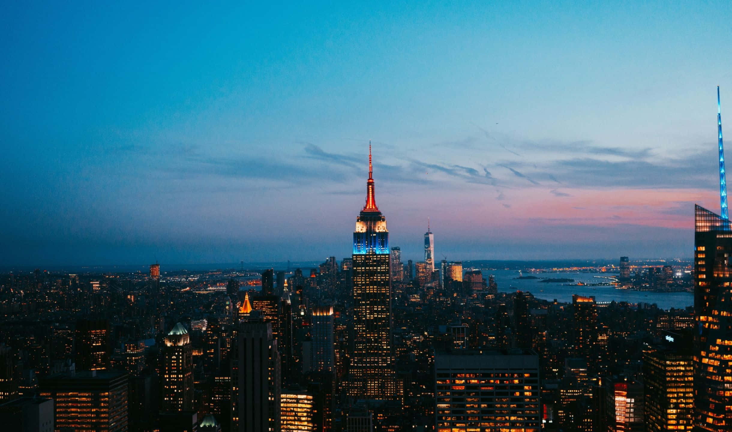 2440x1440 Empire State Building 桌布 壁紙 — 紐約市天際線在黃昏時分，帝國大廈在藍色和粉紅色的漸變天空中亮起。