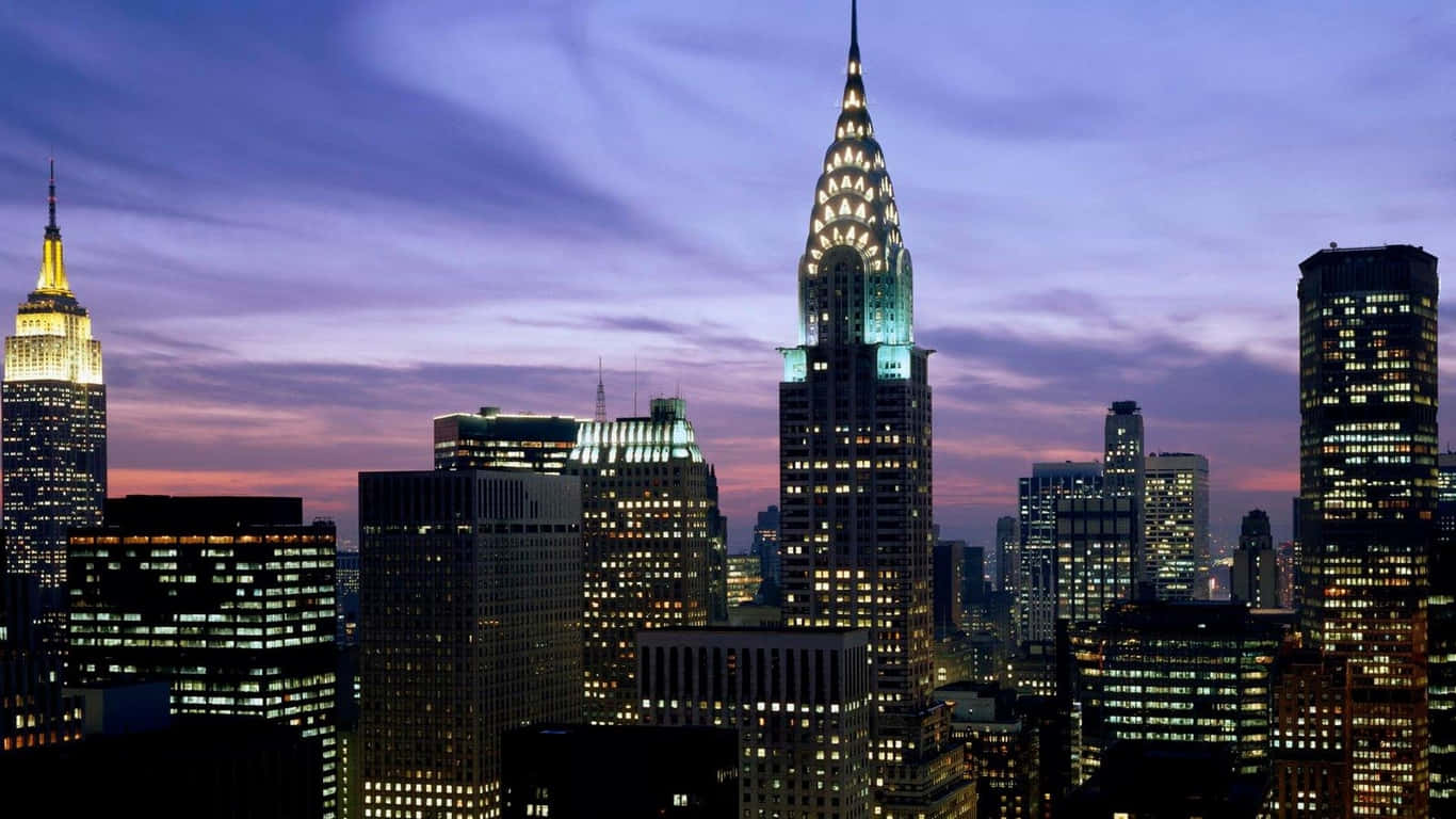 1366x768 Empire State Building 桌布 壁紙 — 紐約市天際線在黃昏時分，摩天大樓燈火通明，映襯著紫色和橙色的天空。