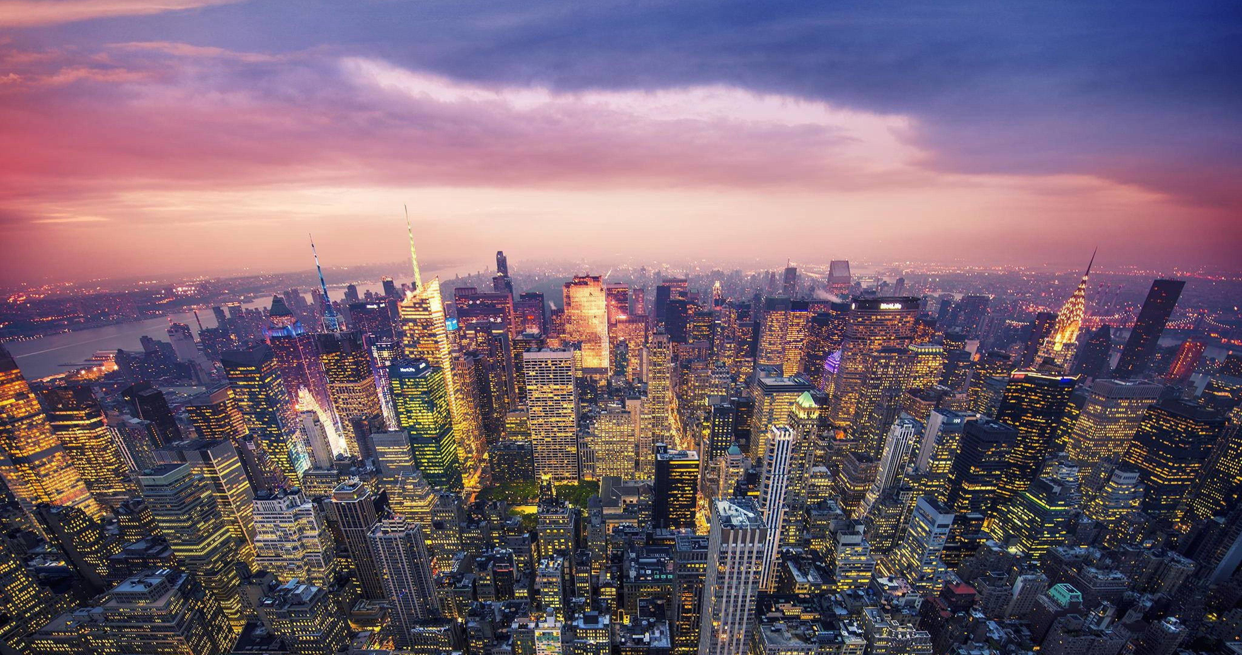 New York 桌布 壁紙 — 紐約市天際線在黃昏時的鳥瞰圖，發光的摩天大樓和粉紫色雲彩在上方。