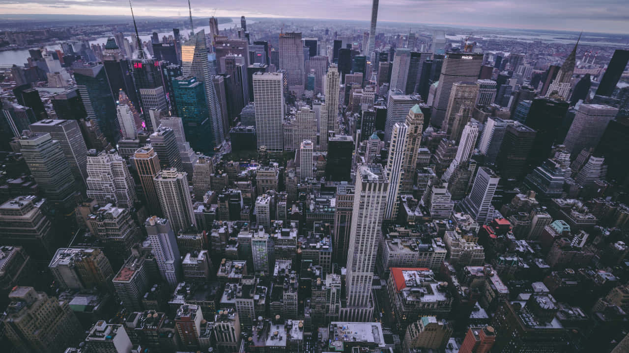 720p Empire State Building 桌布 壁紙 — 紐約市天際線在黃昏時的鳥瞰圖，高聳的摩天大樓和密集的城市建築在柔和的紫色天空下。