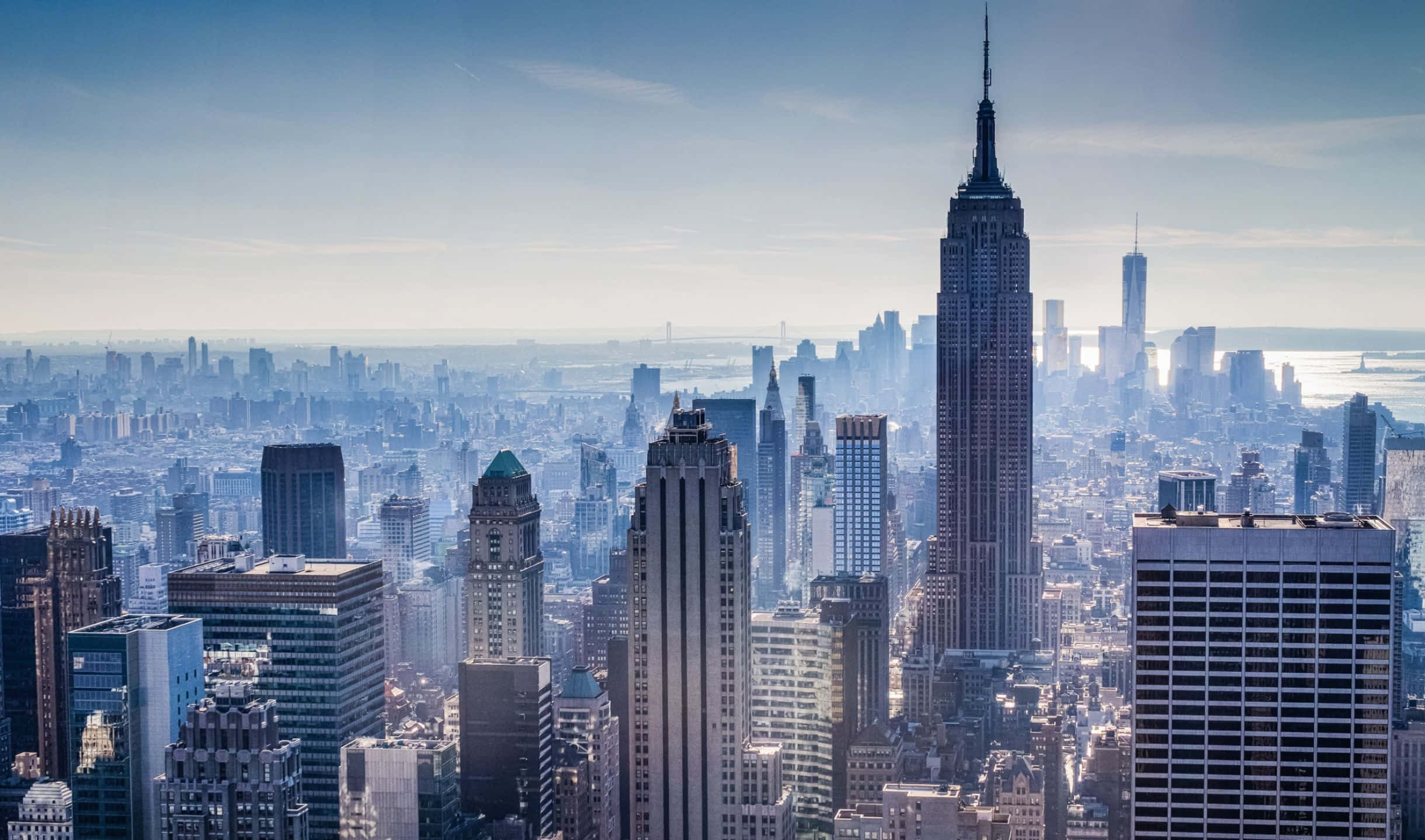 2440x1440 Empire State Building 桌布 壁紙 — 紐約市天際線的全景，帝國大廈在晴朗藍天下高聳於摩天大樓之上。