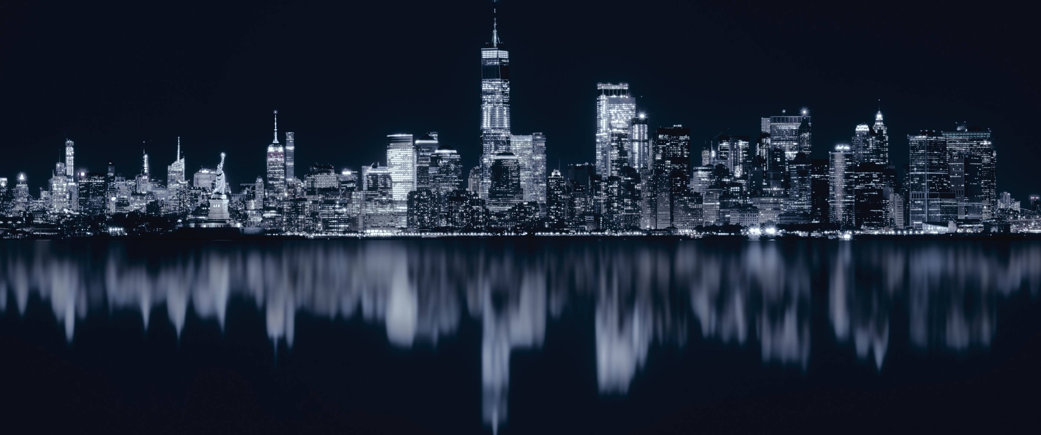 桌布 壁紙 — 紐約市天際線的單色夜景，燈火通明的摩天大樓完美倒映在黑暗的水面上。