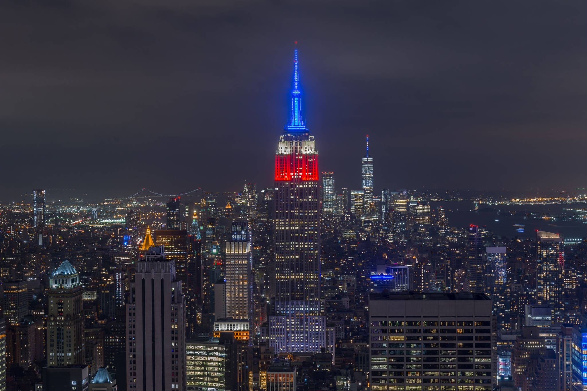 empire state 桌布 壁紙 — 紐約市天際線的壯麗夜景，帝國大廈在黑暗的天空中閃爍著紅色和藍色。