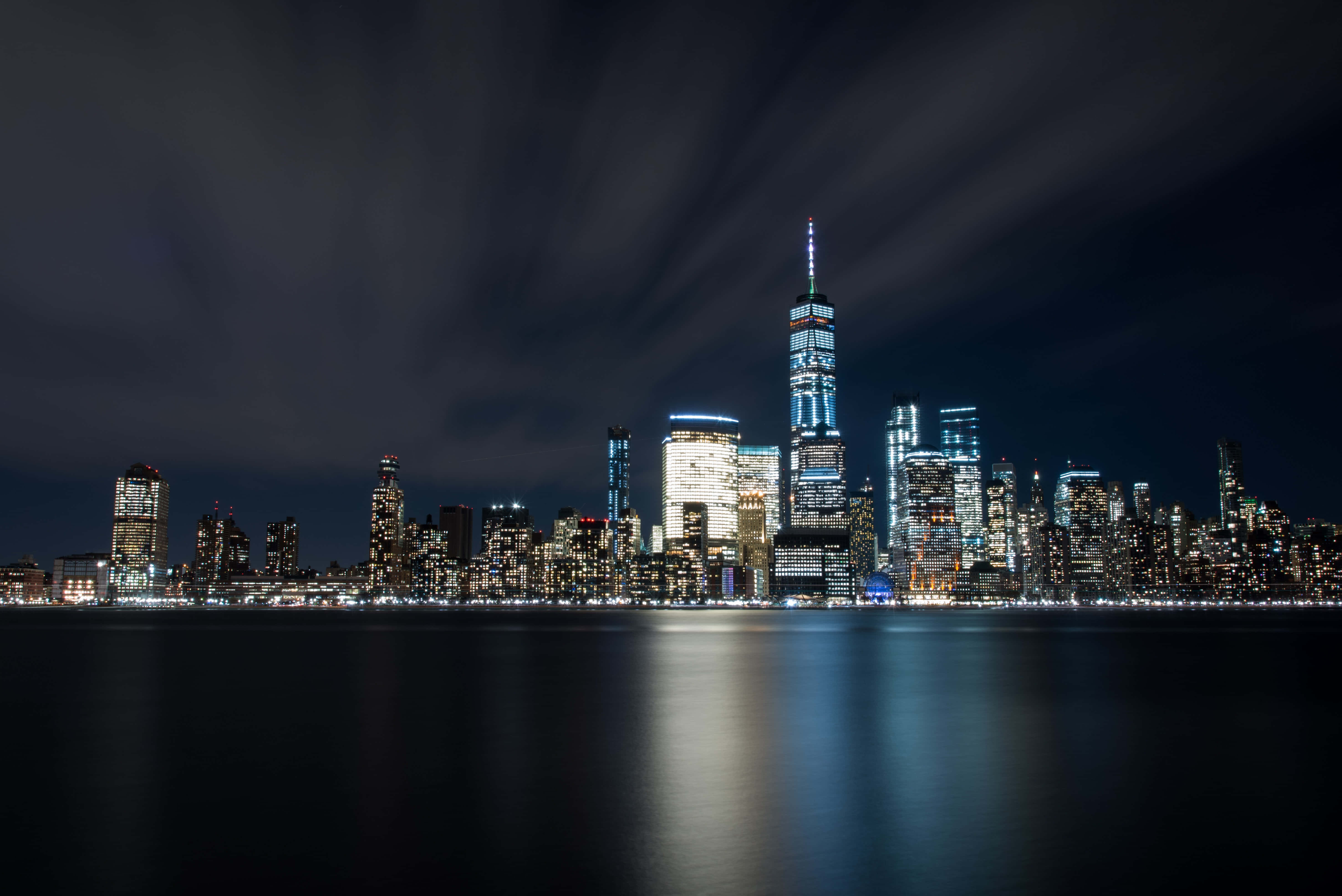 Nyc 桌布 壁紙 — 紐約市天際線的壯麗夜景，摩天大樓在黑暗的天空下照亮，倒映在平靜的水面上。