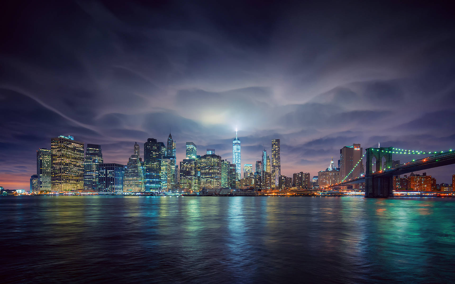 lights 桌布 壁紙 — 紐約市天際線的壯麗夜景，照亮摩天大樓和布魯克林大橋在平靜的水面上倒映，天空有戲劇性的雲層。