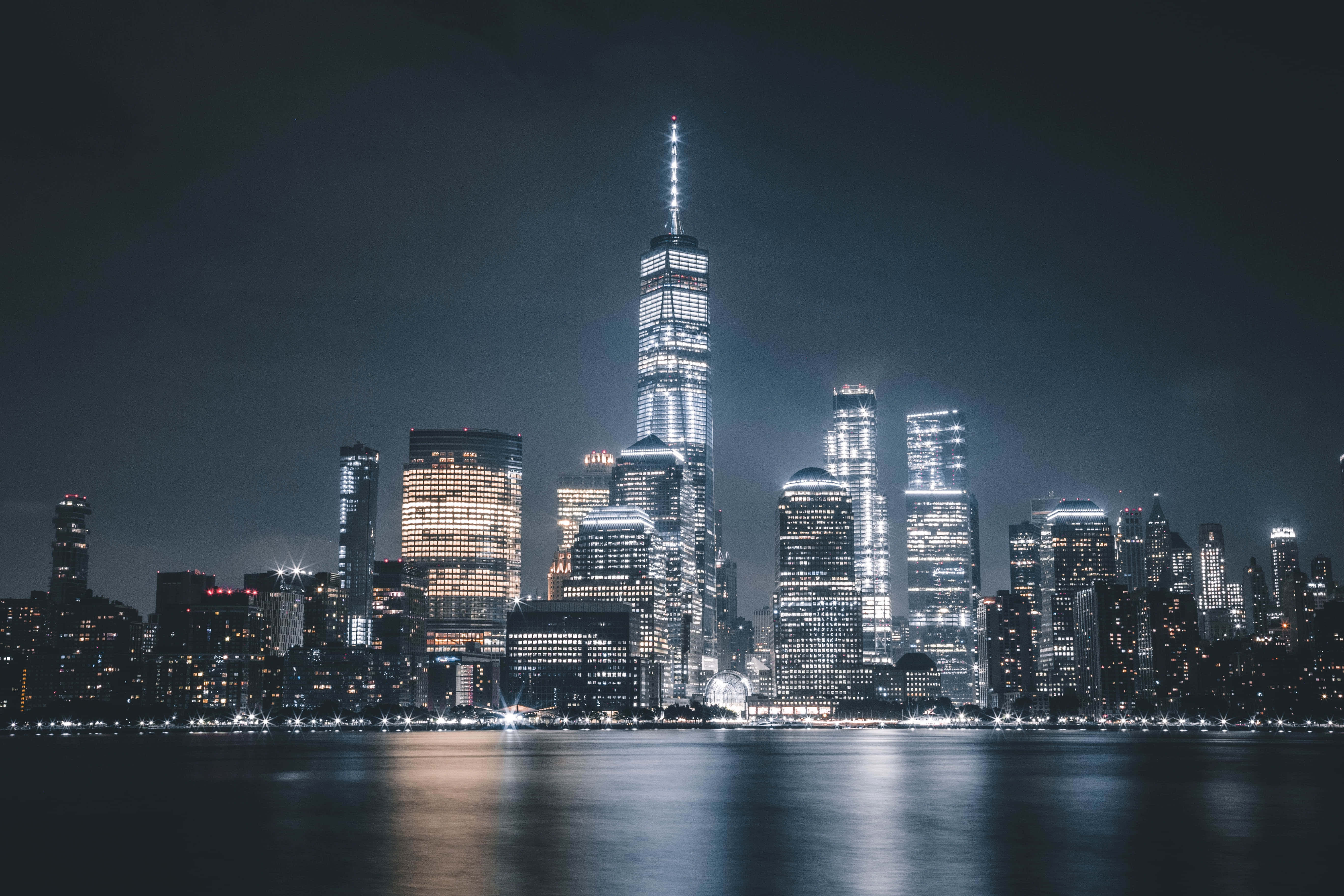 夜空 桌布 壁紙 — 紐約市天際線的壯麗夜景，燈火通明的摩天大樓倒映在平靜的水面上。