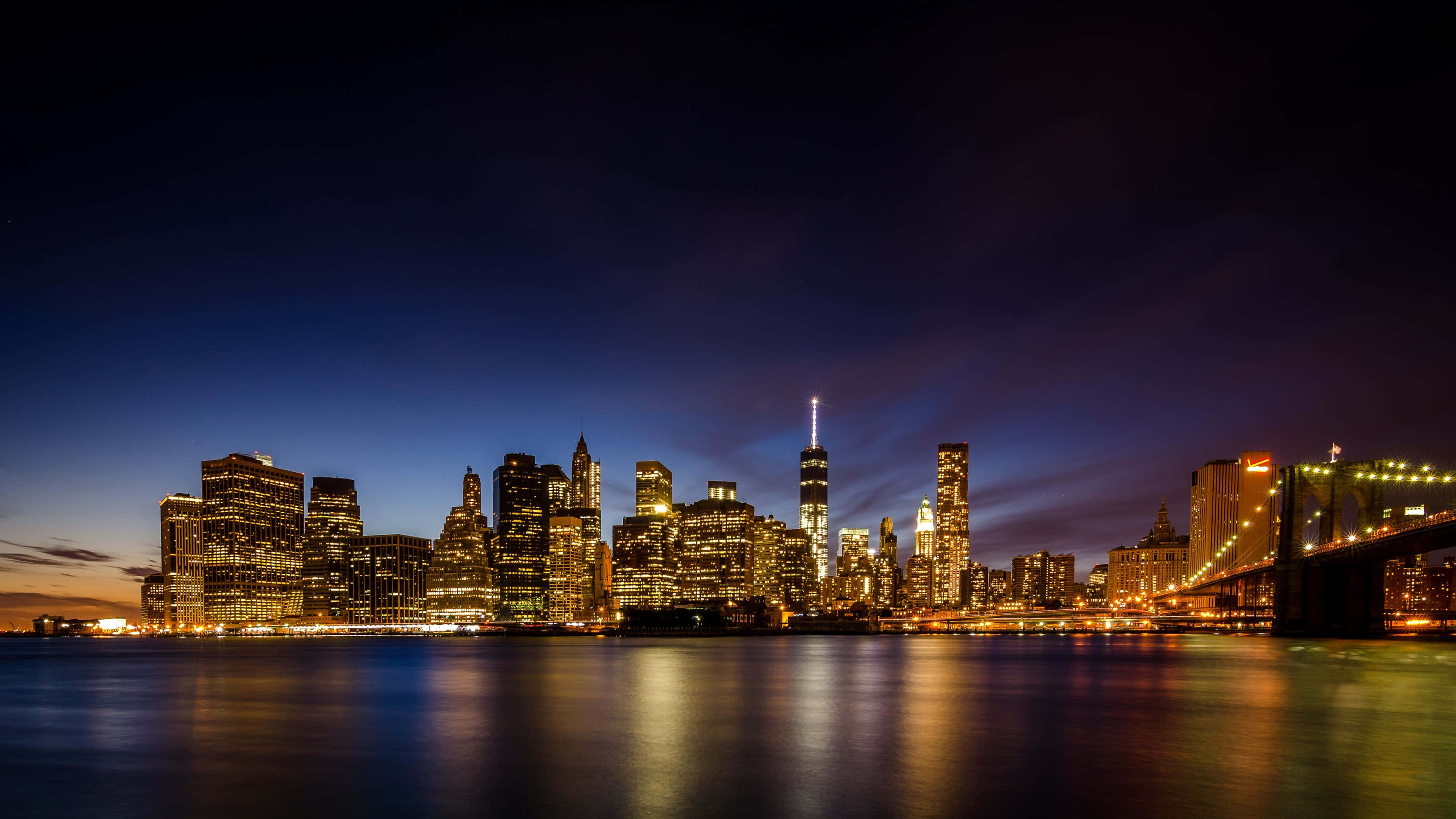 New York City 4K Ultra HD 桌布 壁紙 — 紐約市天際線的壯麗夜景，閃爍的摩天大樓和布魯克林大橋倒映在平靜的水面上。