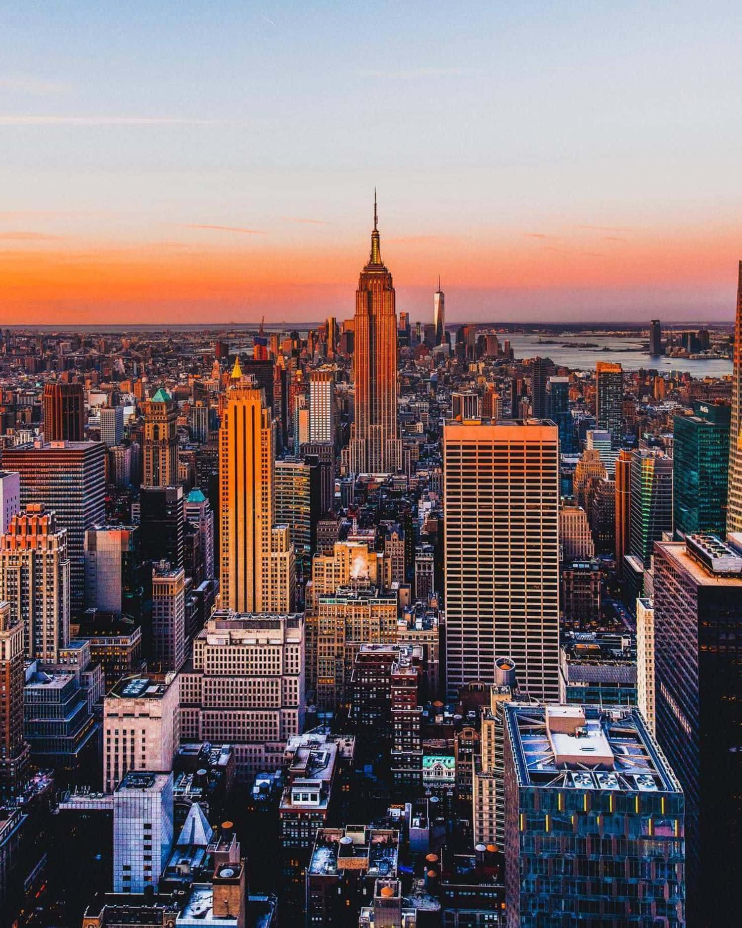Nyc Aesthetic 桌布 壁紙 — 紐約市天際線的壯麗日落，帝國大廈在橙色天空下閃耀琥珀色光芒。