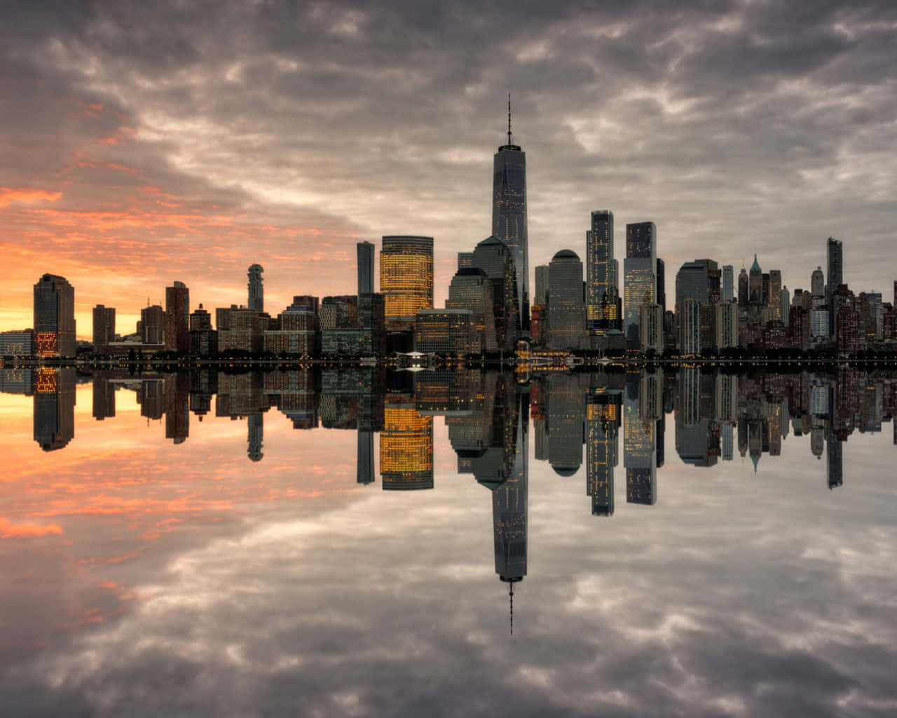 Nyc 桌布 壁紙 — 紐約市天際線的壯麗日落，摩天大樓在平靜的水面上完美倒映，天空佈滿戲劇性的橙色和灰色雲彩。