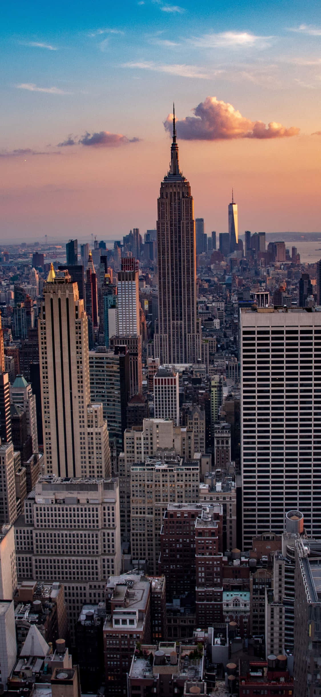 New York 桌布 壁紙 — 紐約市天際線的壯麗日落景觀，以帝國大廈為主導，上方有溫暖的粉紅色和橙色雲彩。