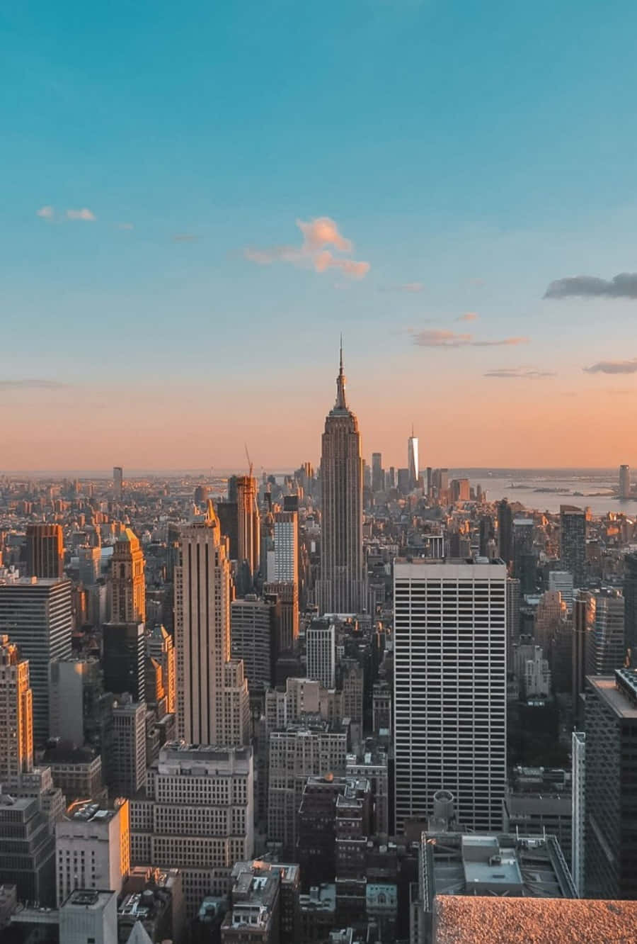 Nyc Aesthetic 桌布 壁紙 — 紐約市天際線的壯麗日落景觀，帝國大廈在柔和粉紅和藍色天空的映襯下閃耀著金色光芒。