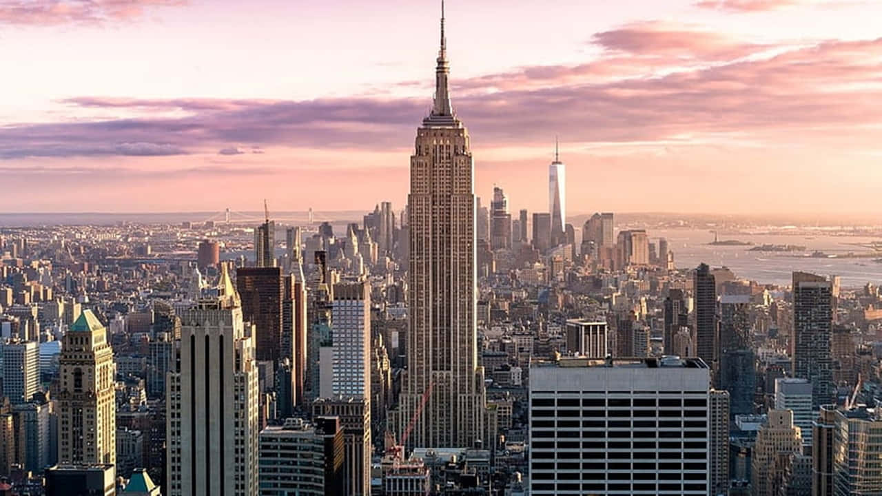 720p Ny City 桌布 壁紙 — 紐約市天際線的壯麗日落景觀，帝國大廈聳立於密集的城市建築和遠處的水面之上。