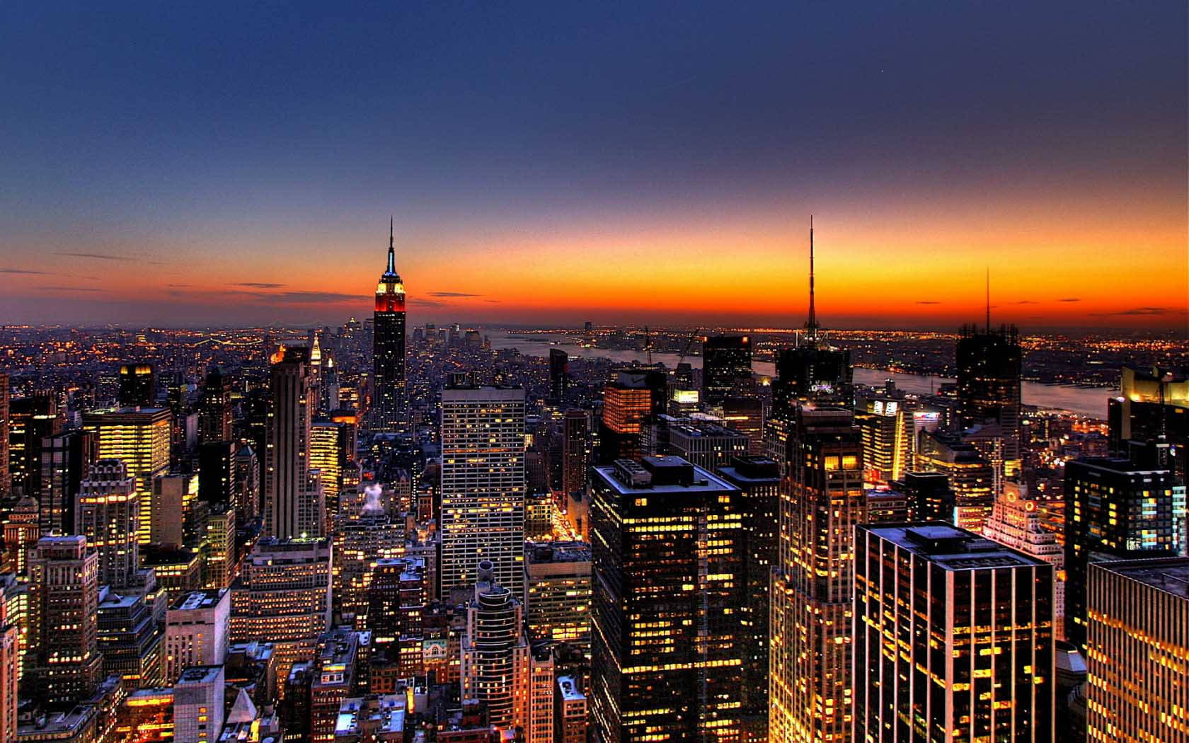New York 桌布 壁紙 — 紐約市天際線的壯麗暮色景觀，摩天大樓在鮮豔的橙色和深藍色天空下閃閃發光。