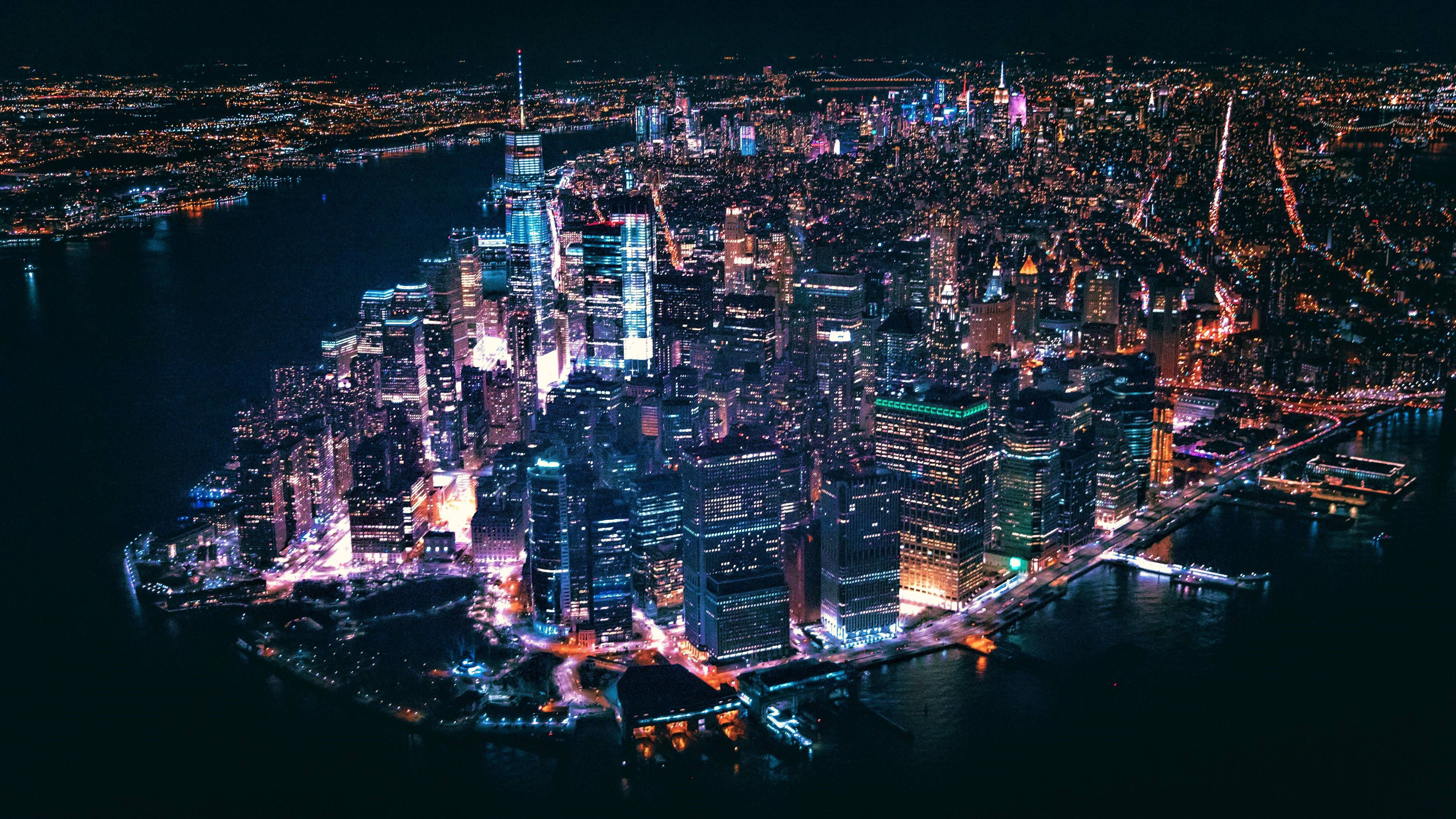 lights 桌布 壁紙 — 紐約市天際線的夜間空中景觀，閃爍著鮮豔的霓虹燈光，倒映在黑暗的水面上。