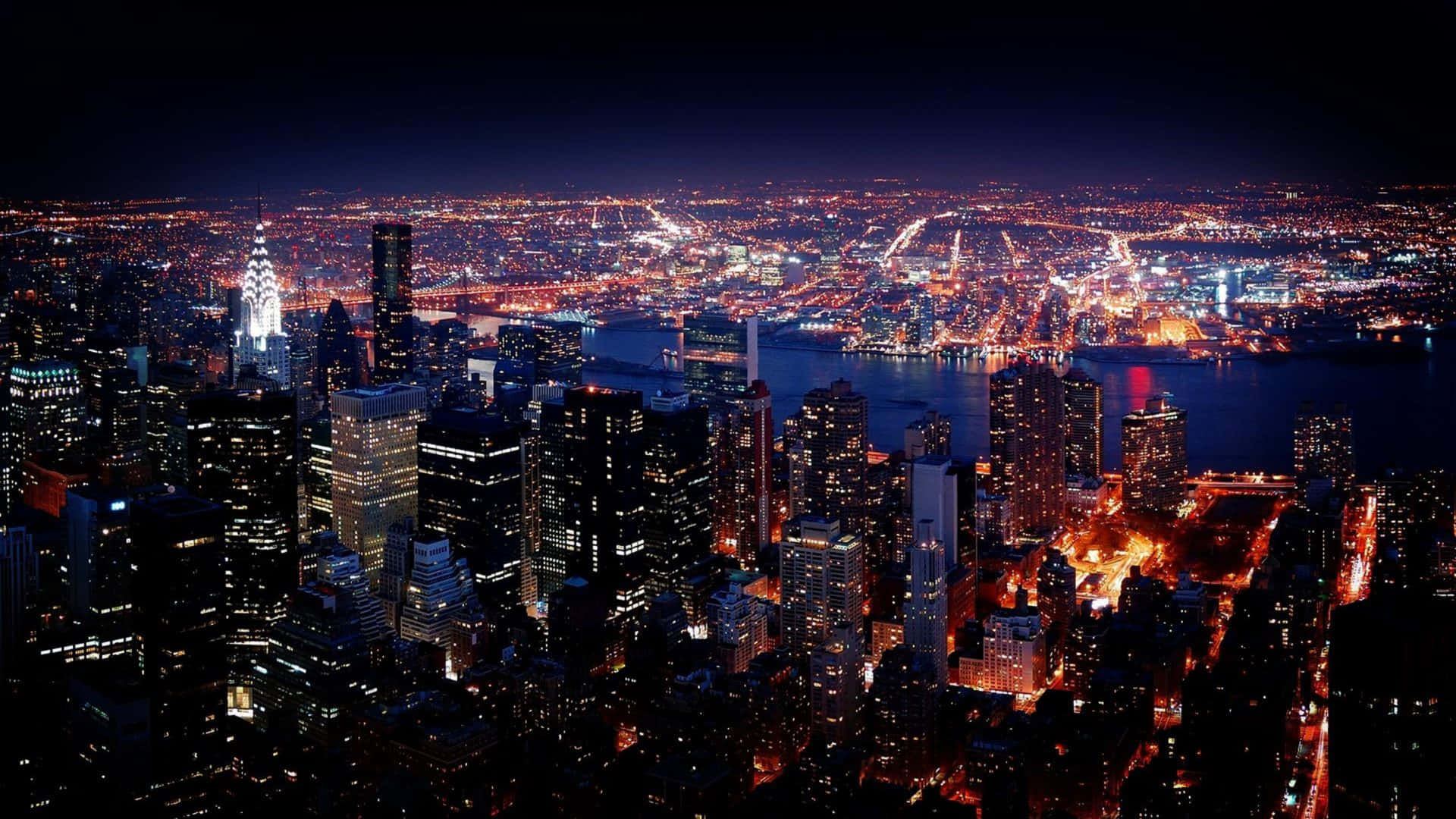 Buildings 桌布 壁紙 — 紐約市天際線的夜間空中景觀，閃爍的摩天大樓和河流反射城市燈光。