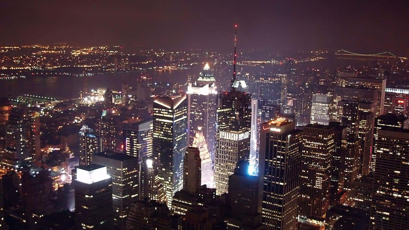 1366x768 Empire State Building 桌布 壁紙 — 紐約市天際線的夜間空中景觀，高樓大廈燈火通明，遠處的橋樑在黑暗的天空下閃耀。