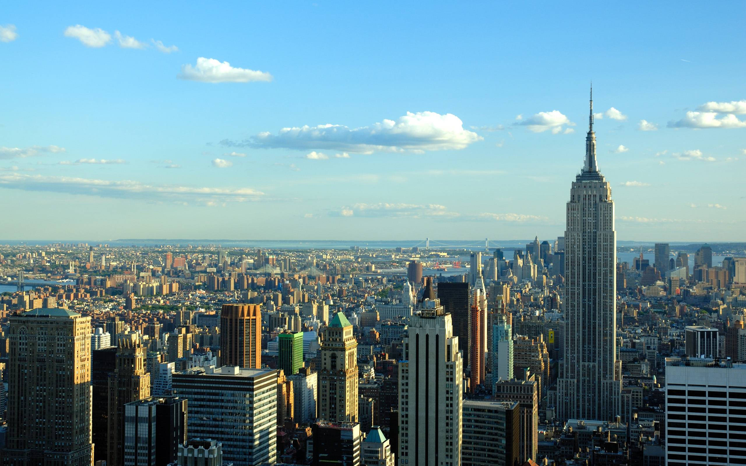 New York City Desktop 桌布 壁紙 — 紐約市天際線的廣闊日間景觀，以帝國大廈為主導，天空湛藍，雲朵稀疏。
