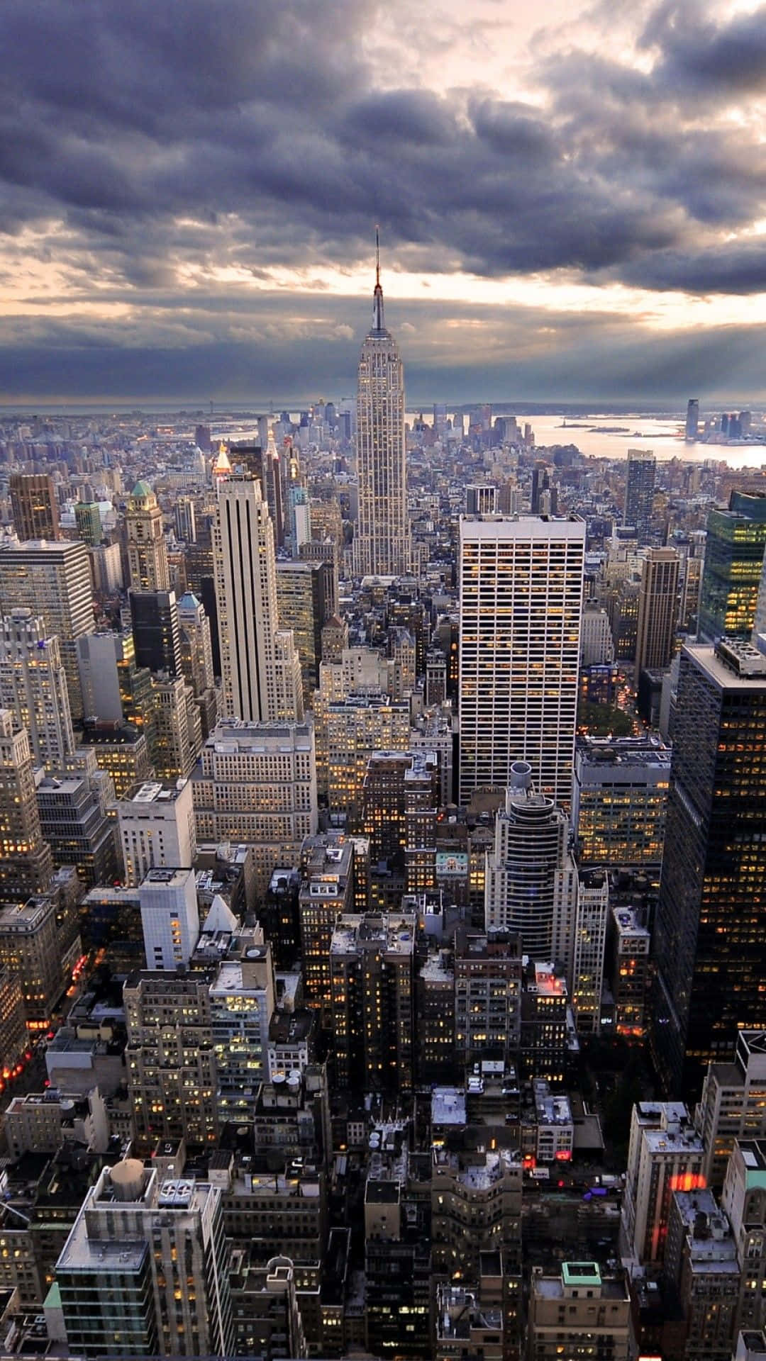 iPhone Xs New York 桌布 壁紙 — 紐約市天際線的戲劇性暮色景觀，帝國大廈在暴風雲下聳立於密集的城市建築之上。